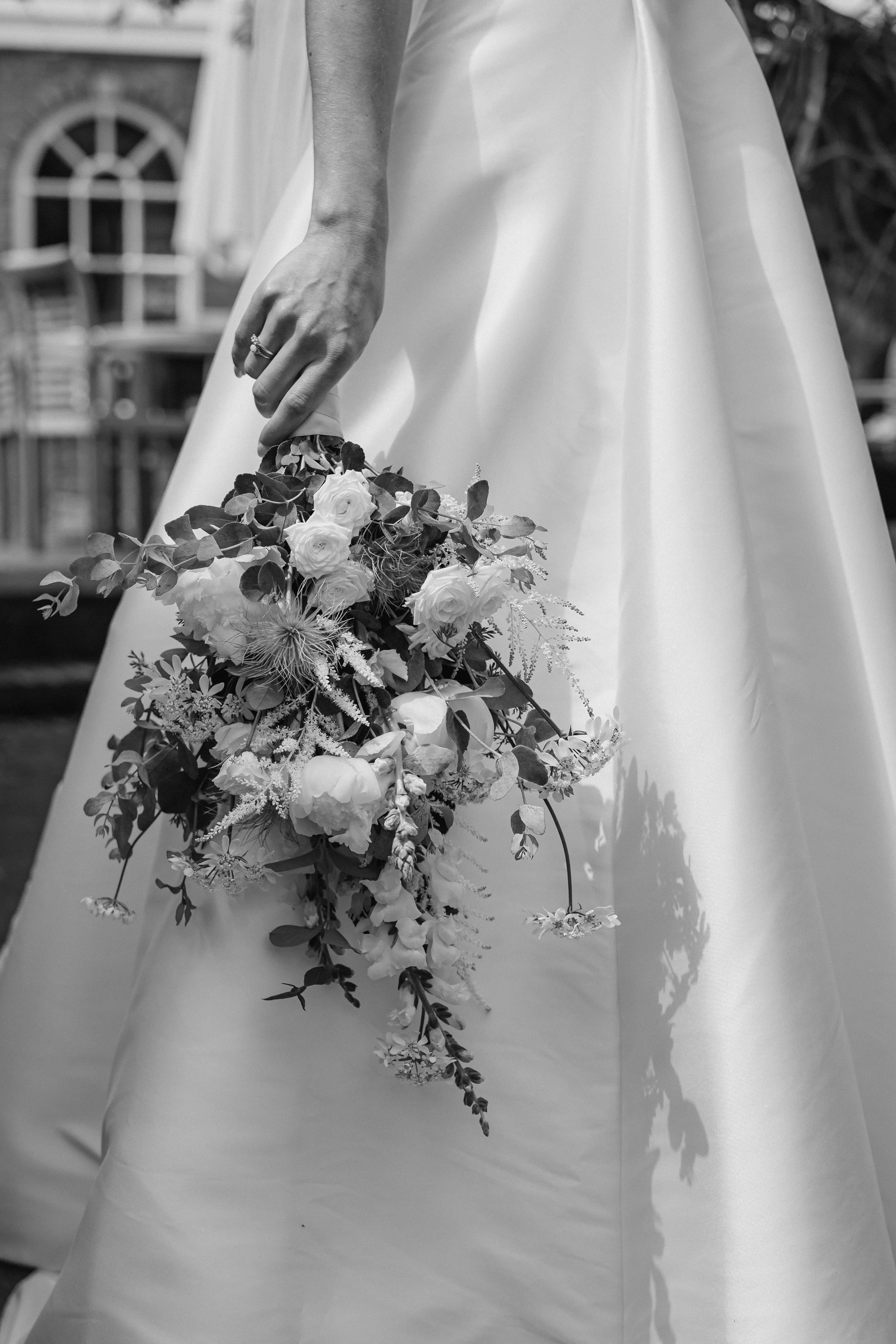 A bride in a wedding dress holding a cascading bouquet of flowers and greenery.