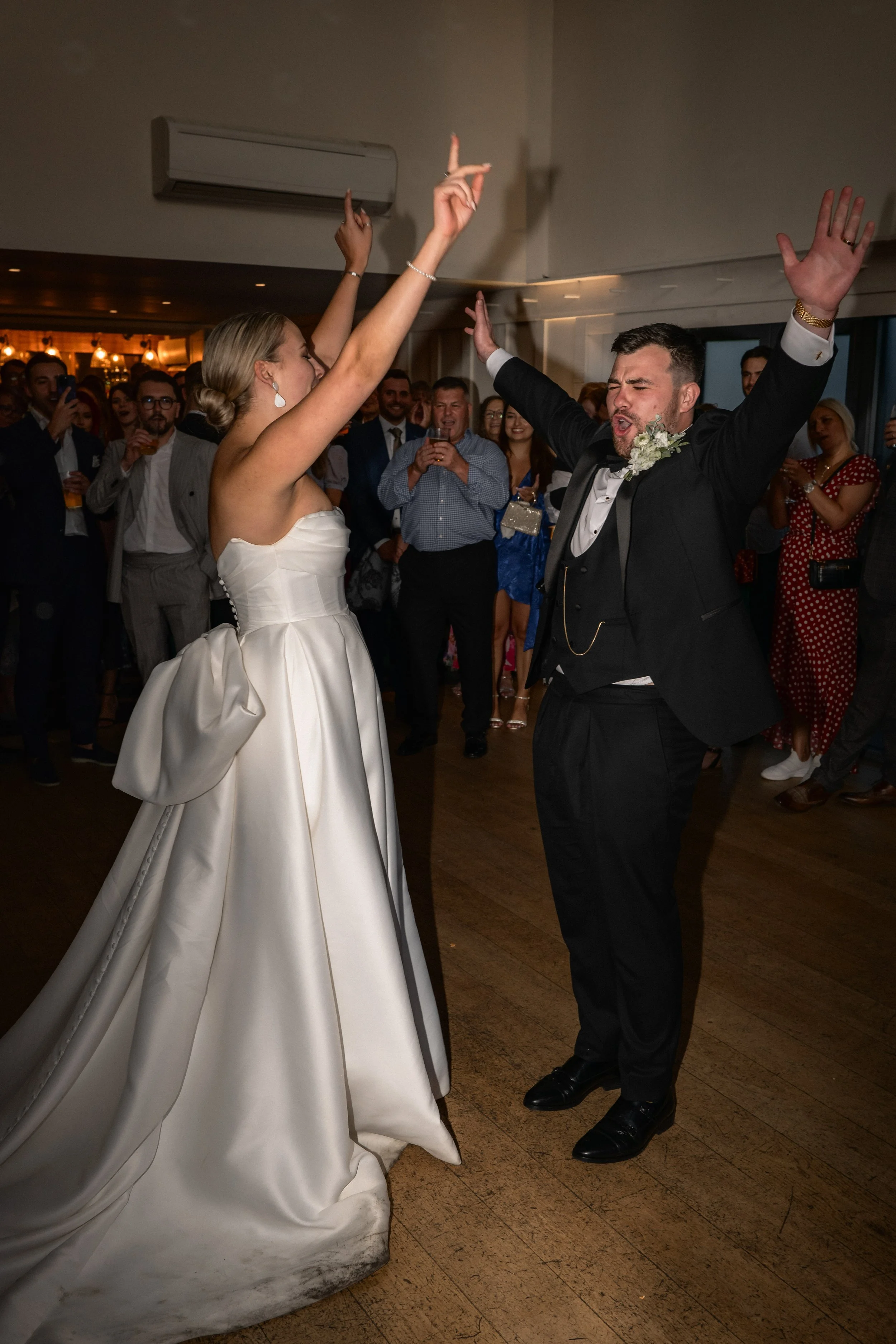 Bride and groom dancing at wedding reception with guests watching and celebrating.