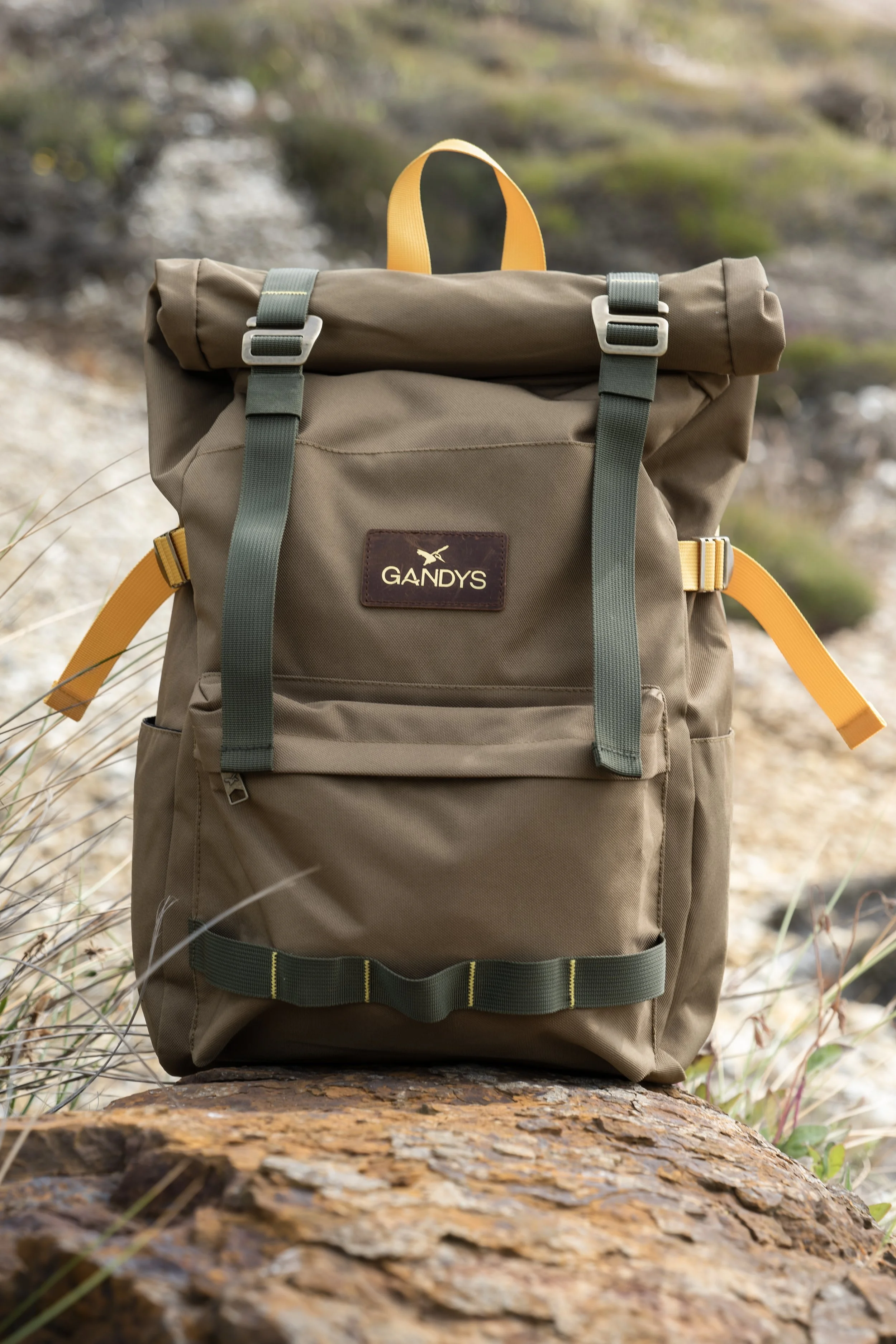 Olive green GANDYS backpack resting on a log outdoors.