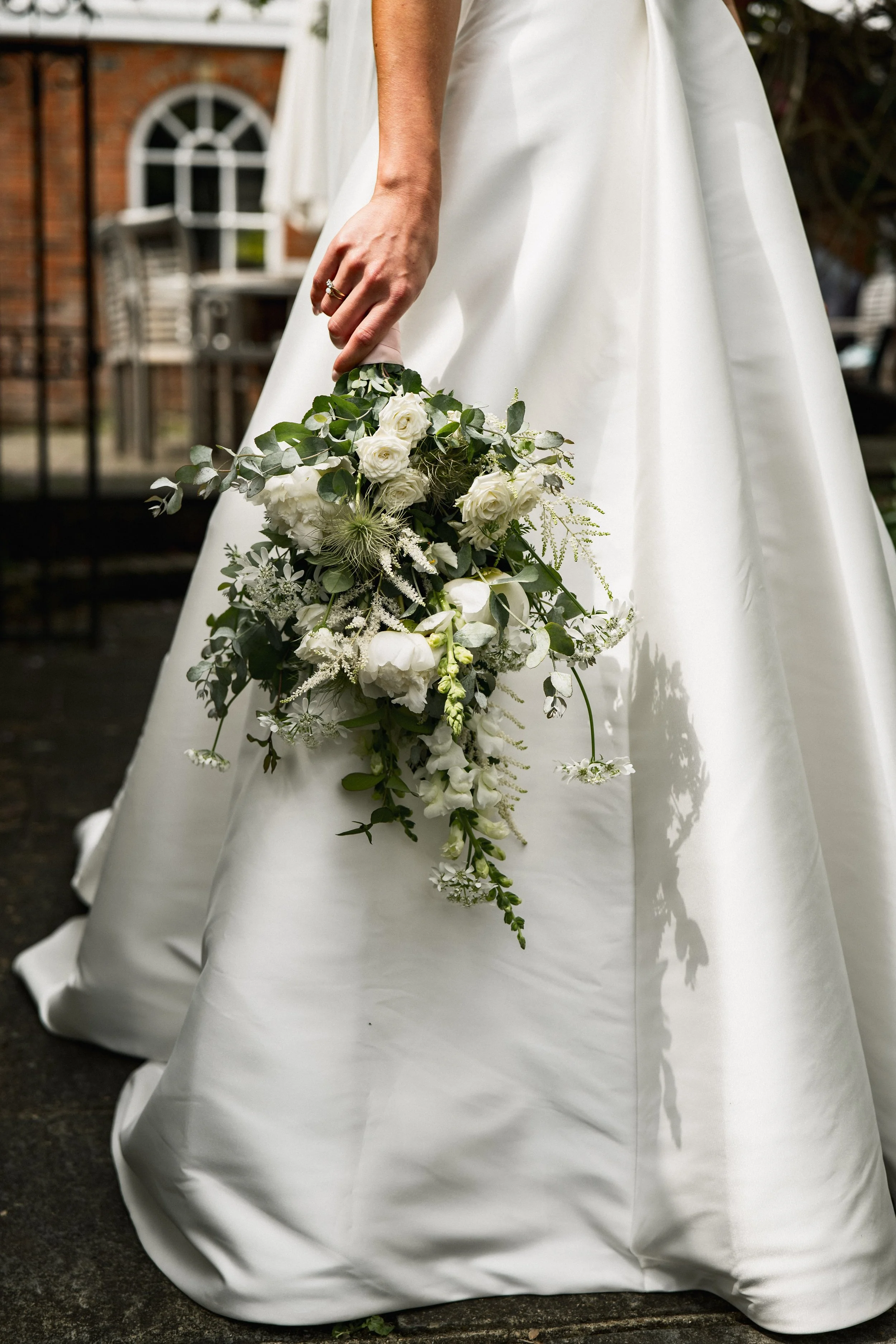 A bride in a white wedding gown holding a cascading bouquet of white flowers and greenery.