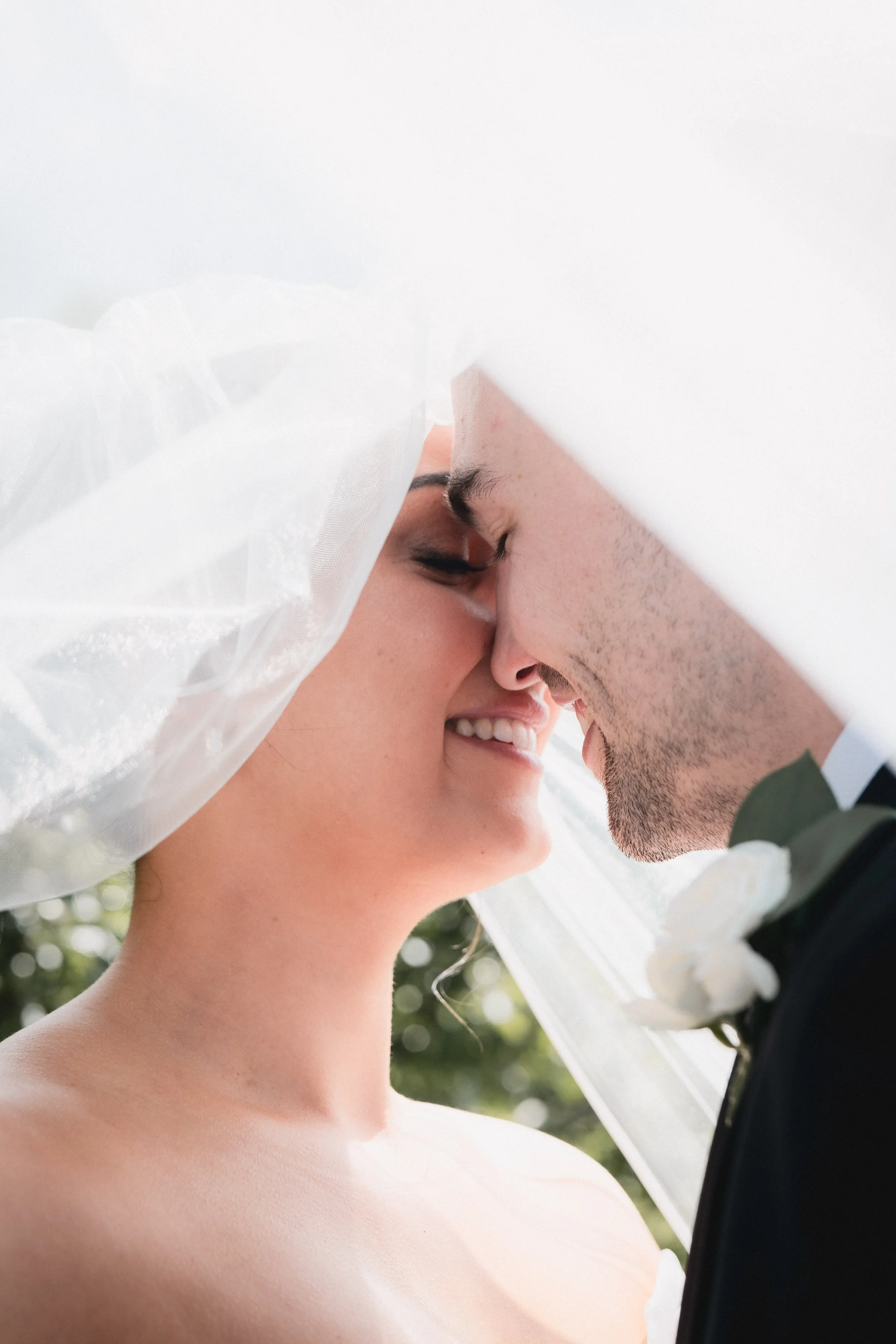 A bride and groom with their foreheads touching under a veil
