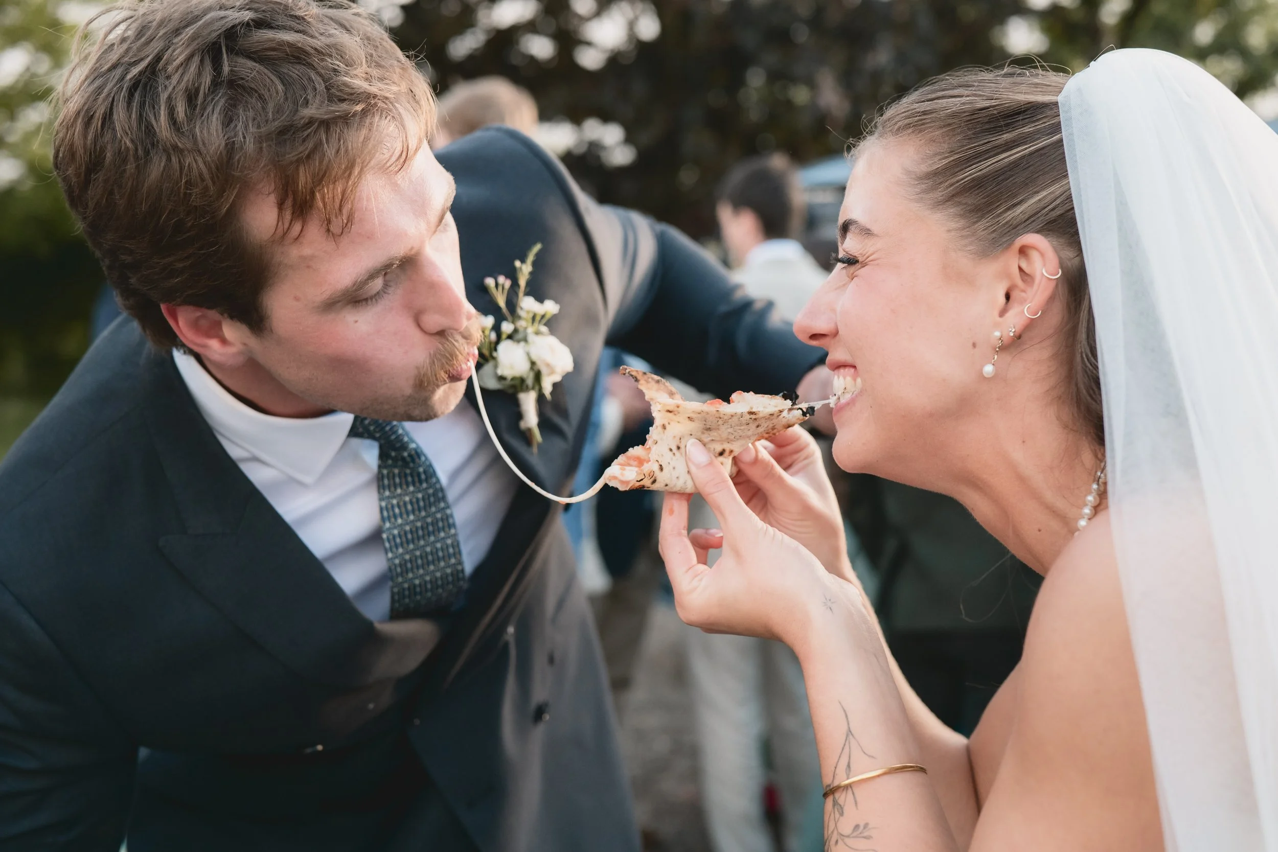 A bride and groom sharing a slice of pizza at their wedding celebration outdoors.