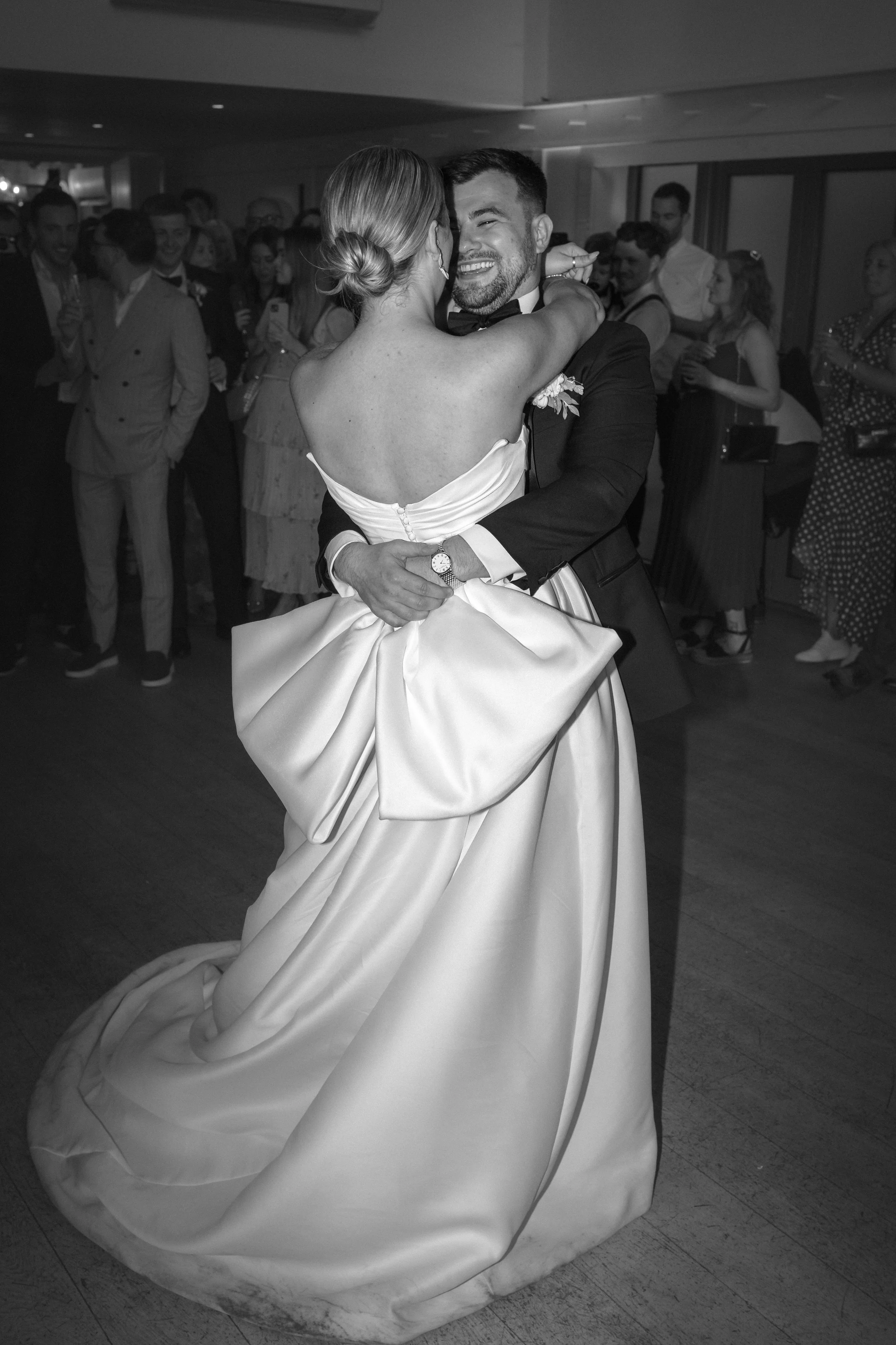 A bride and groom sharing a dance at their wedding reception, with guests in the background.