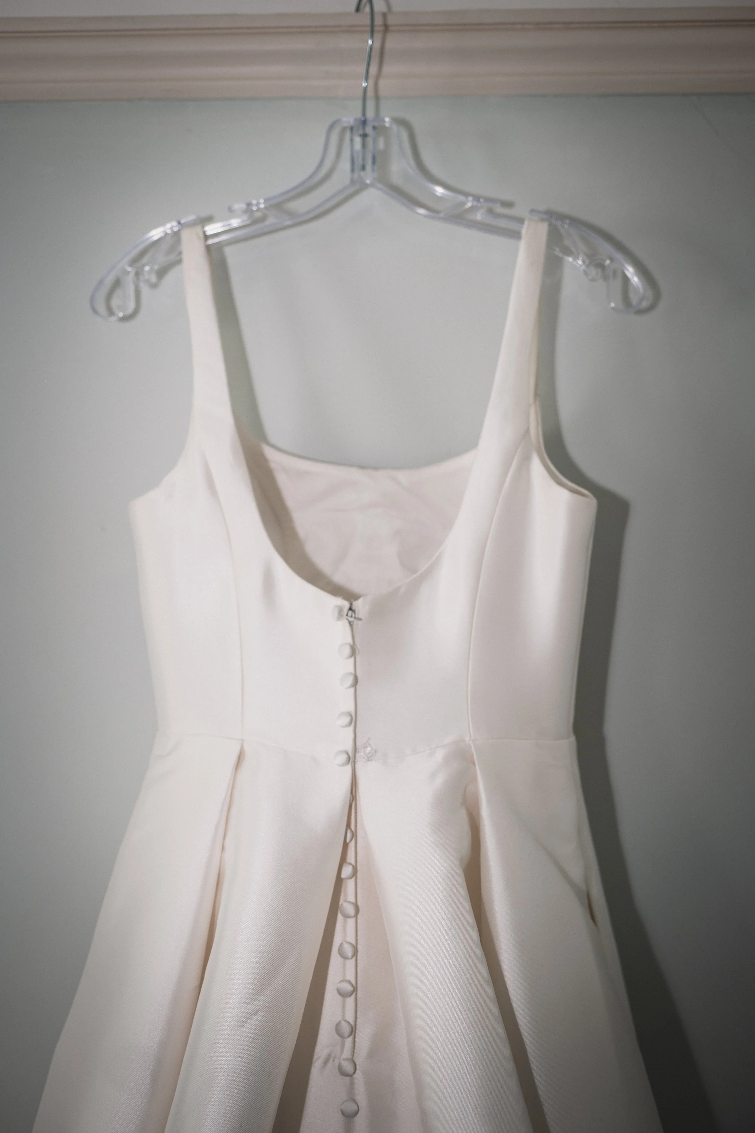 A white wedding dress with buttons down the front, hanging on a hanger.