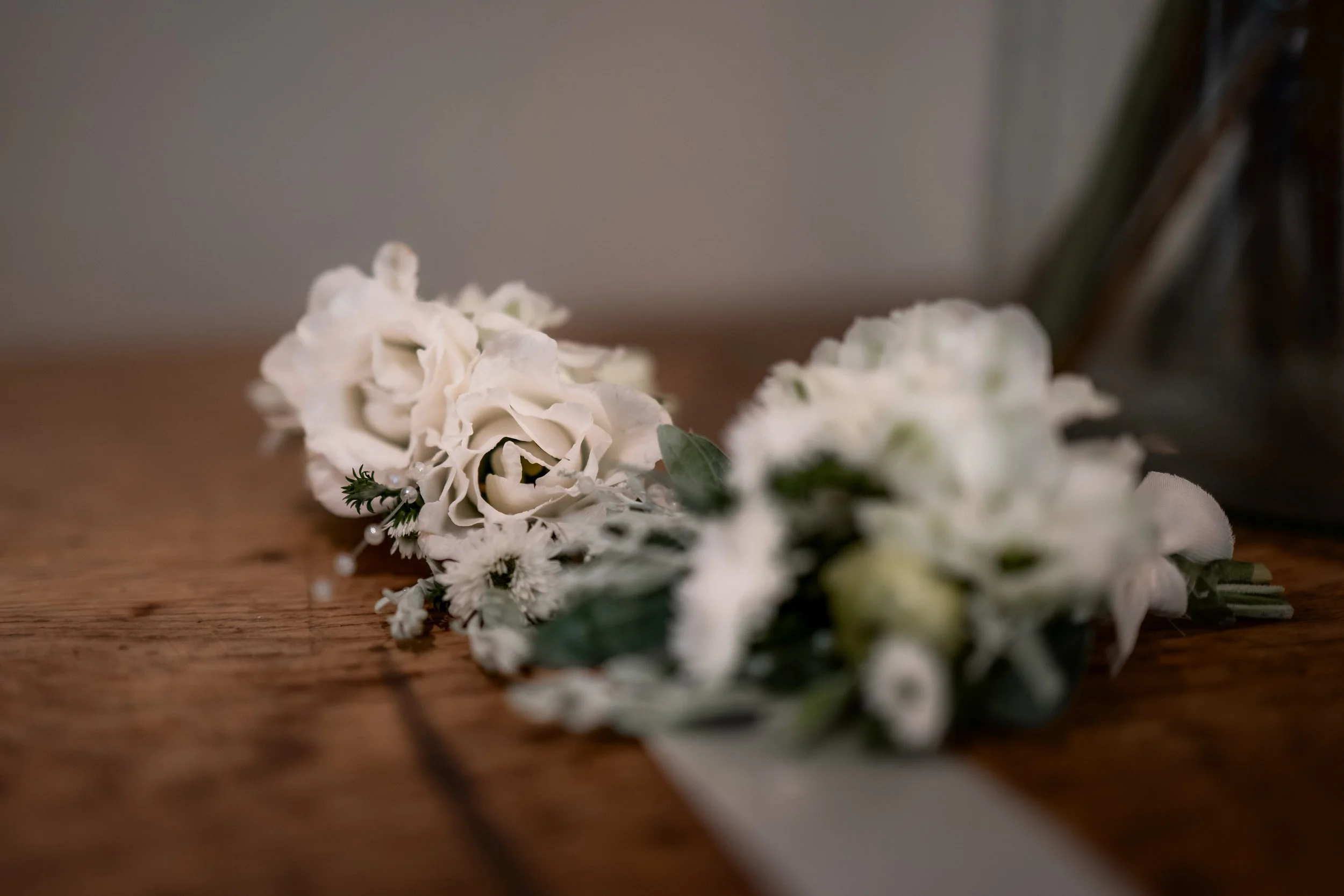 White floral boutonniere with green leaves on a wooden surface.