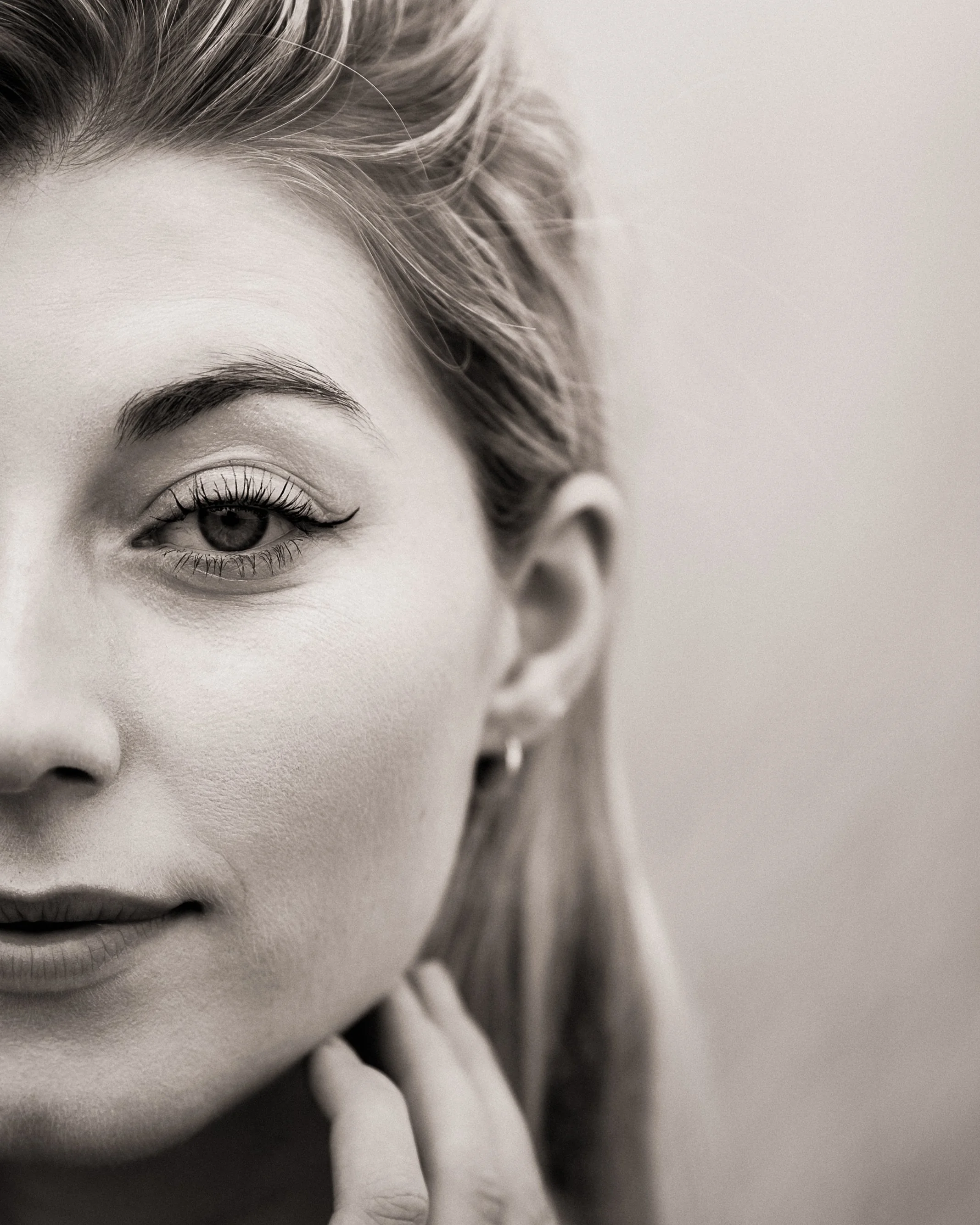 Close-up of a woman's face in black and white, showing her eye, part of her nose, lips, and hand near her chin, with her hair swept back.