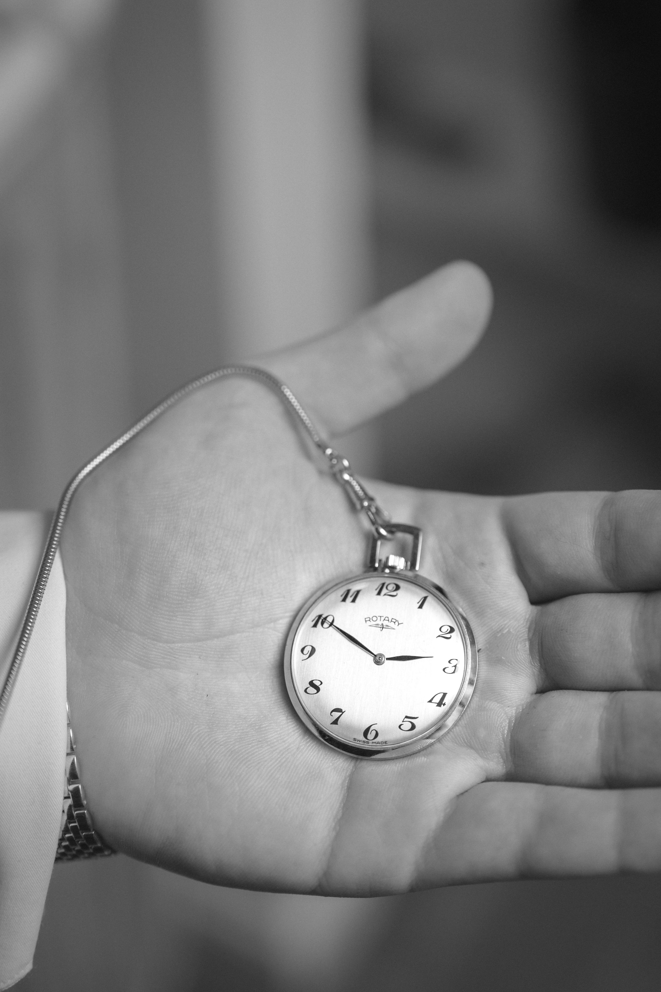 A person holding a pocket watch in their open hand. The watch has a chain attached and displays the time as 2:50.