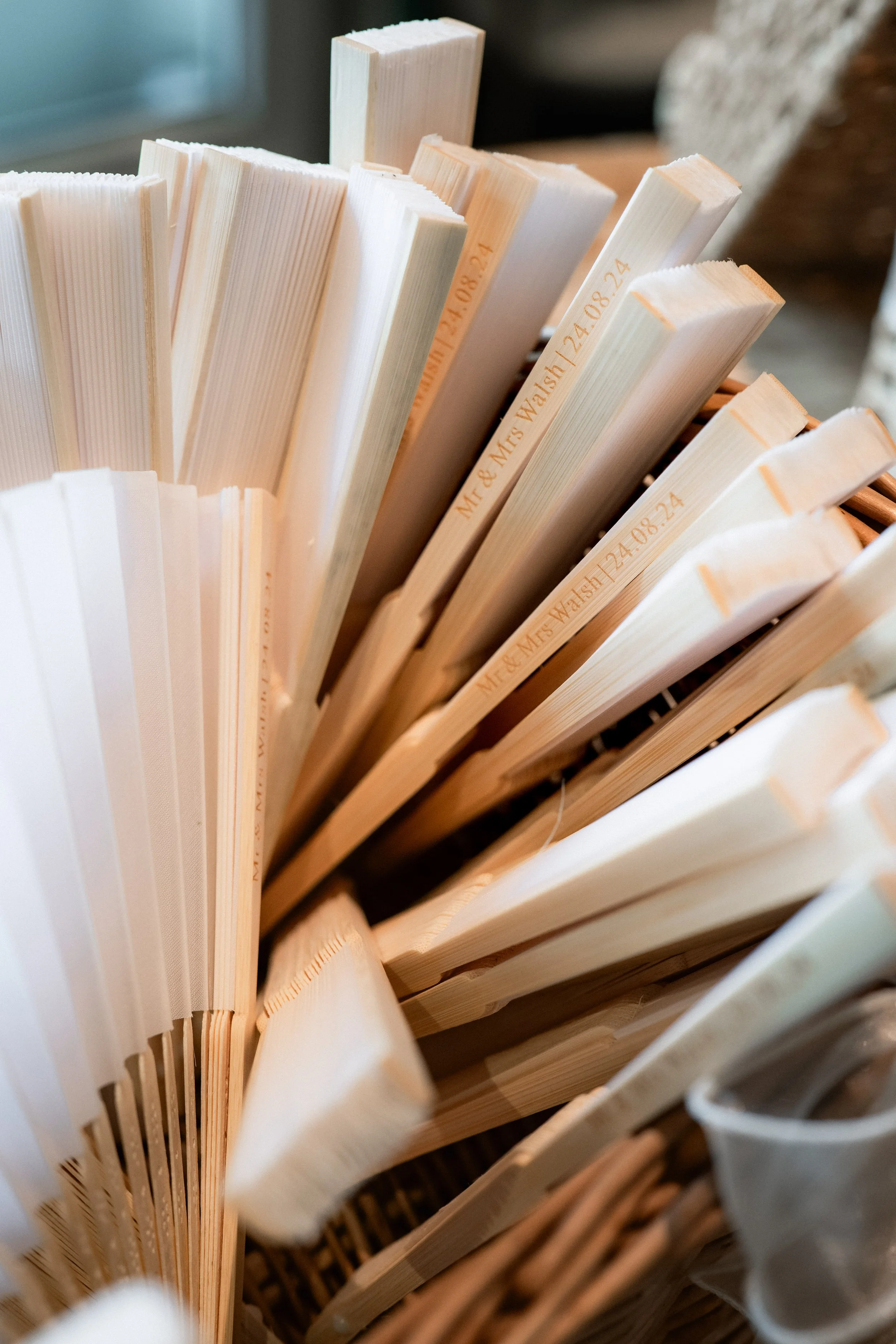 Folded white paper fans with personalized engraving resting in a woven basket.