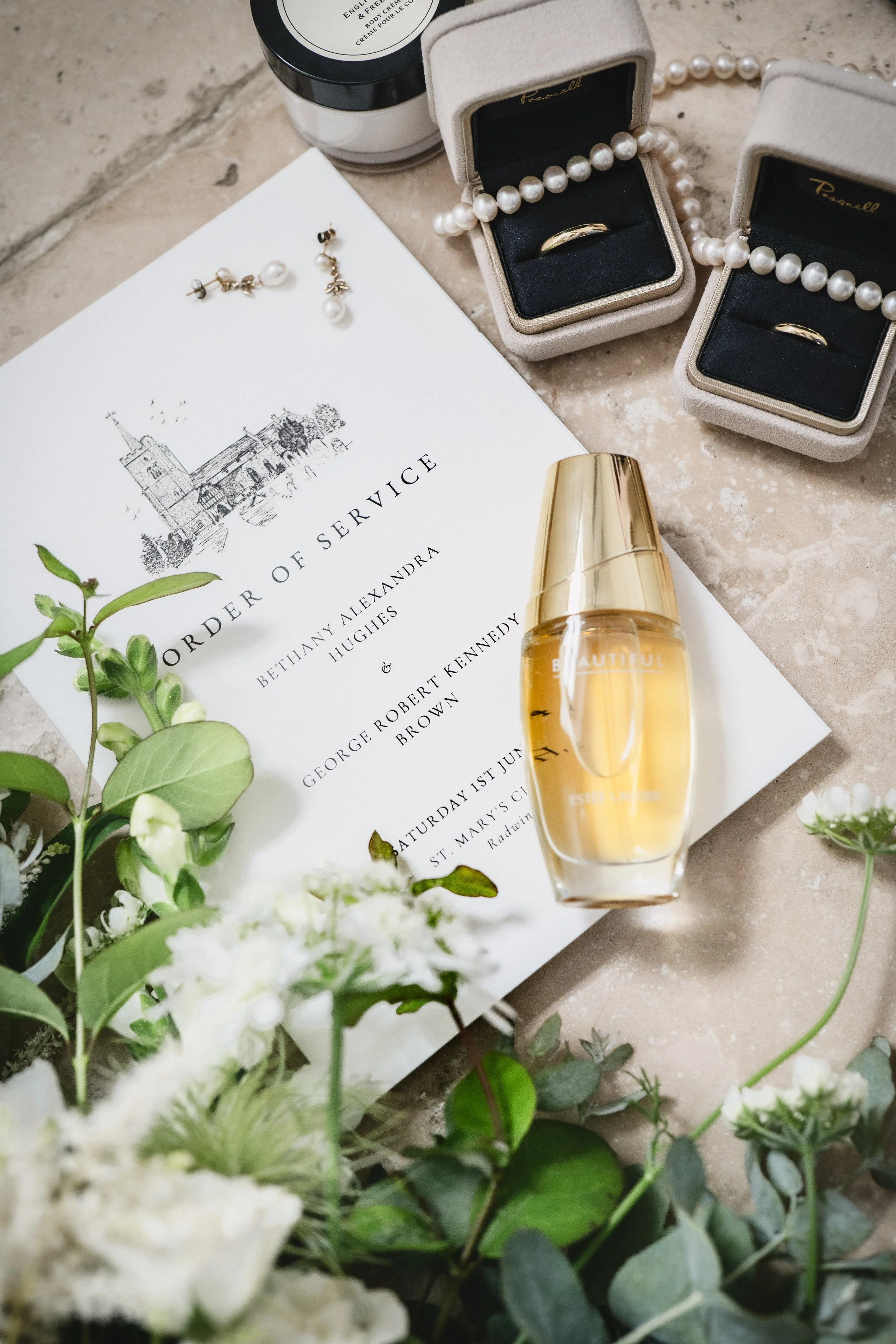 Wedding invitation with pearl jewelry, perfume bottle, and floral decorations.