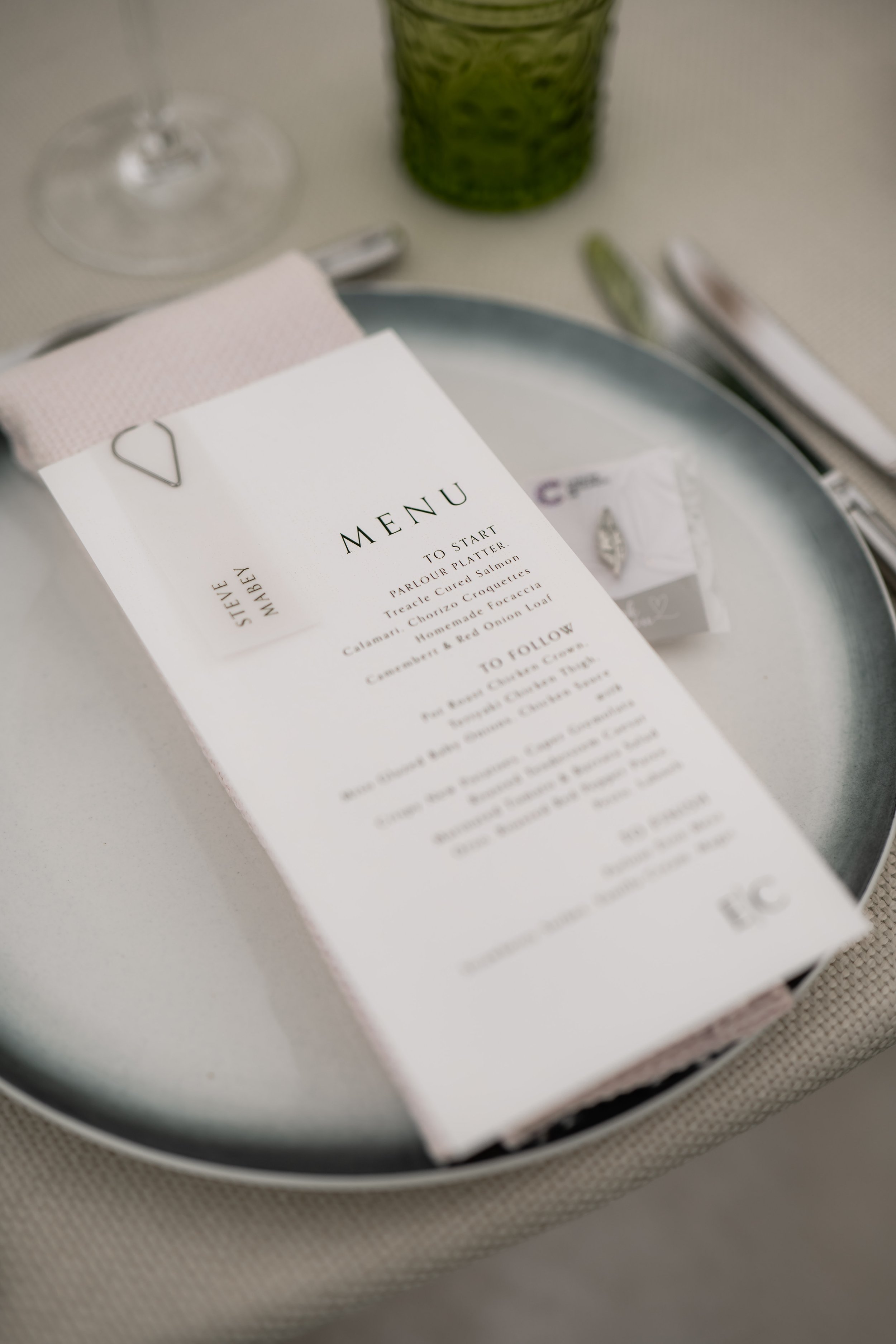 A restaurant table setting with a menu, a wine glass, a napkin, and utensils on a white table.