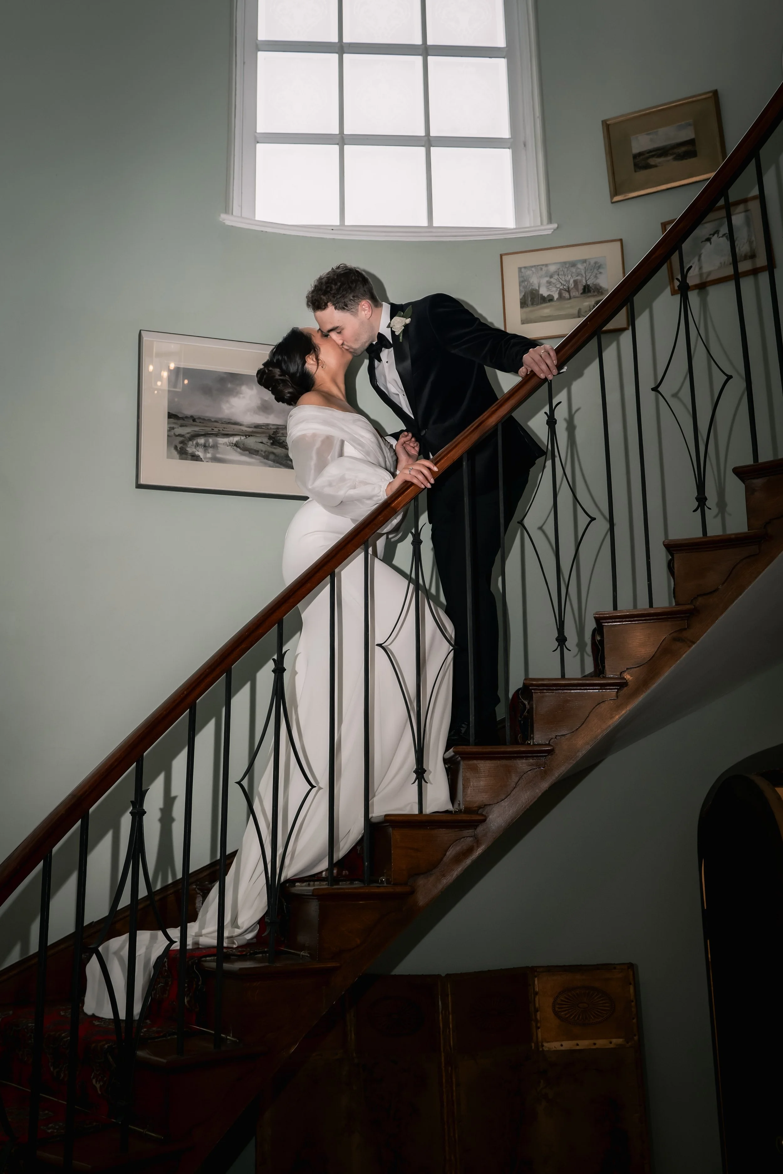 A bride and groom sharing a kiss on a staircase inside a house.