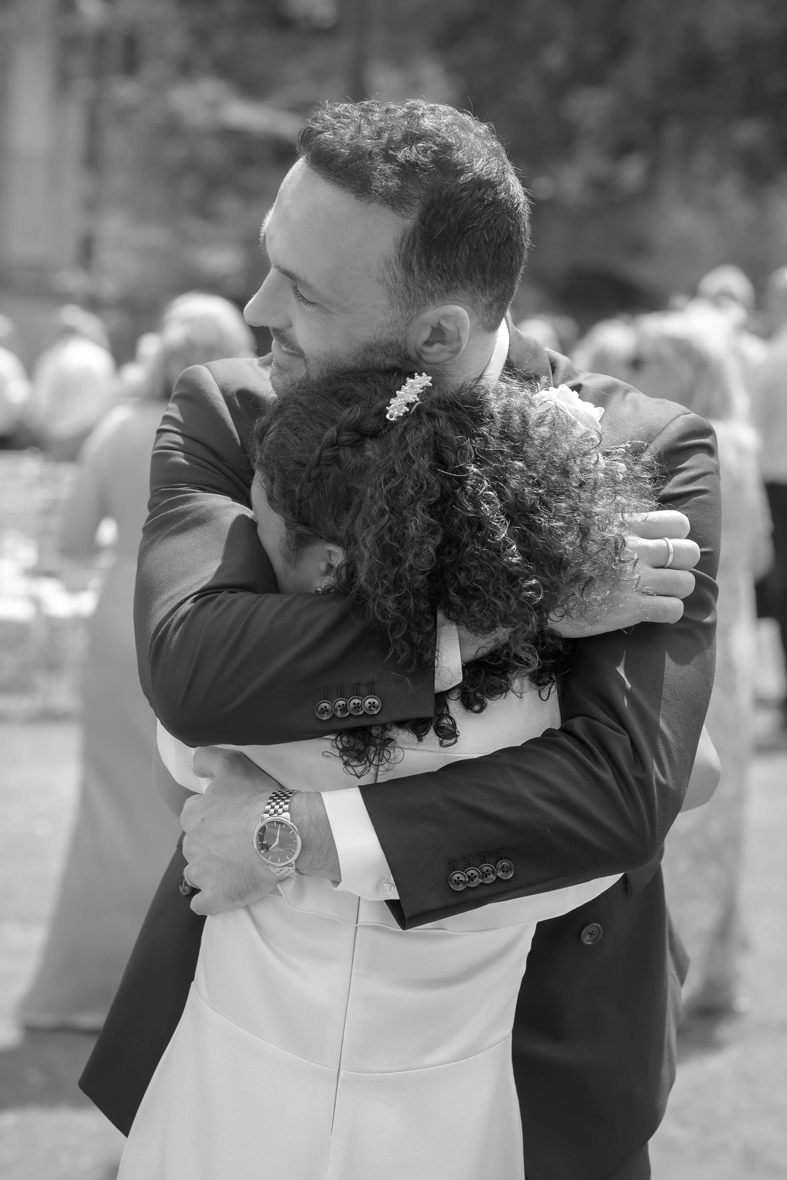 A man in a suit hugging a woman in a dress at an outdoor event.