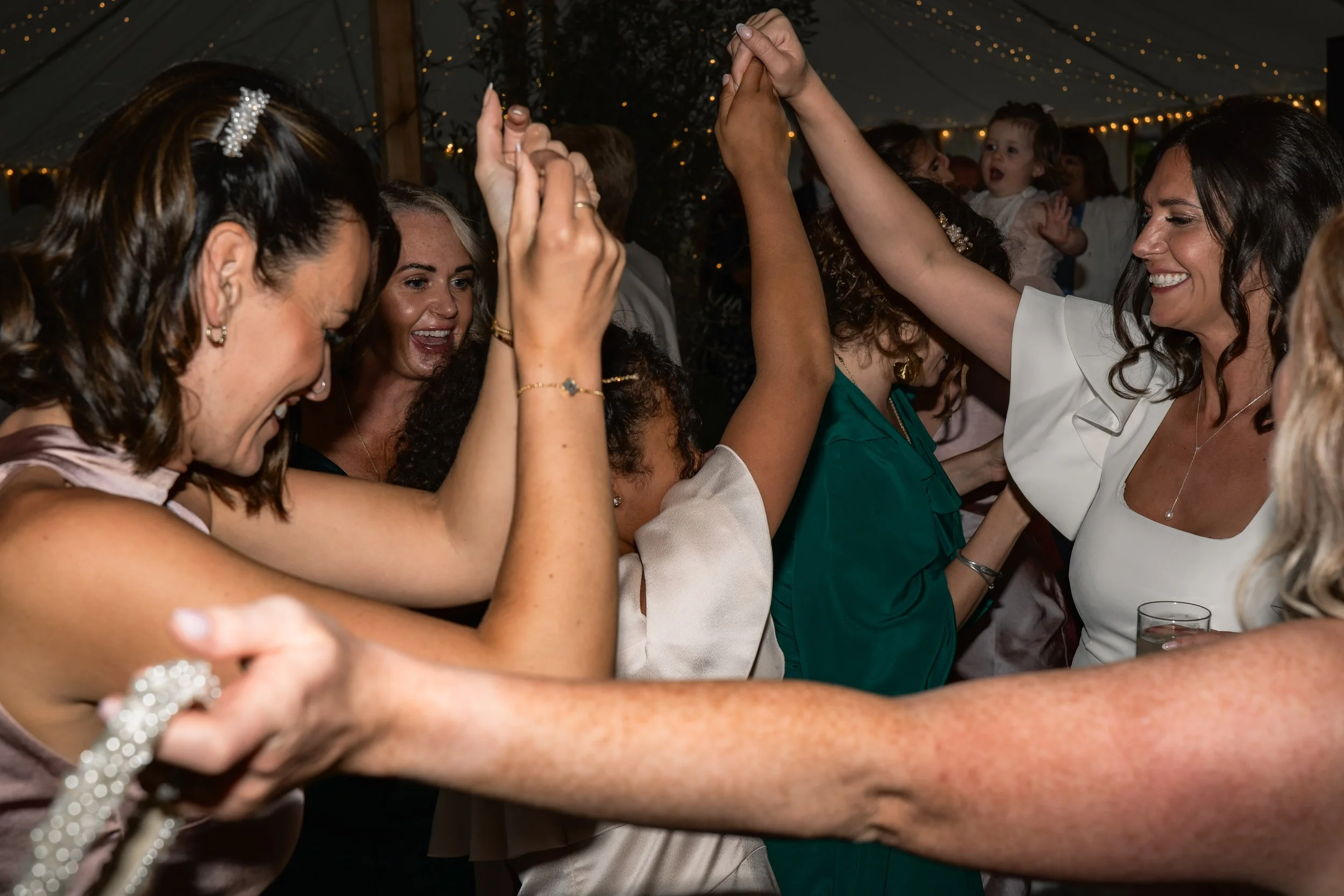 Group of women dancing and celebrating at a party, smiling and holding hands.