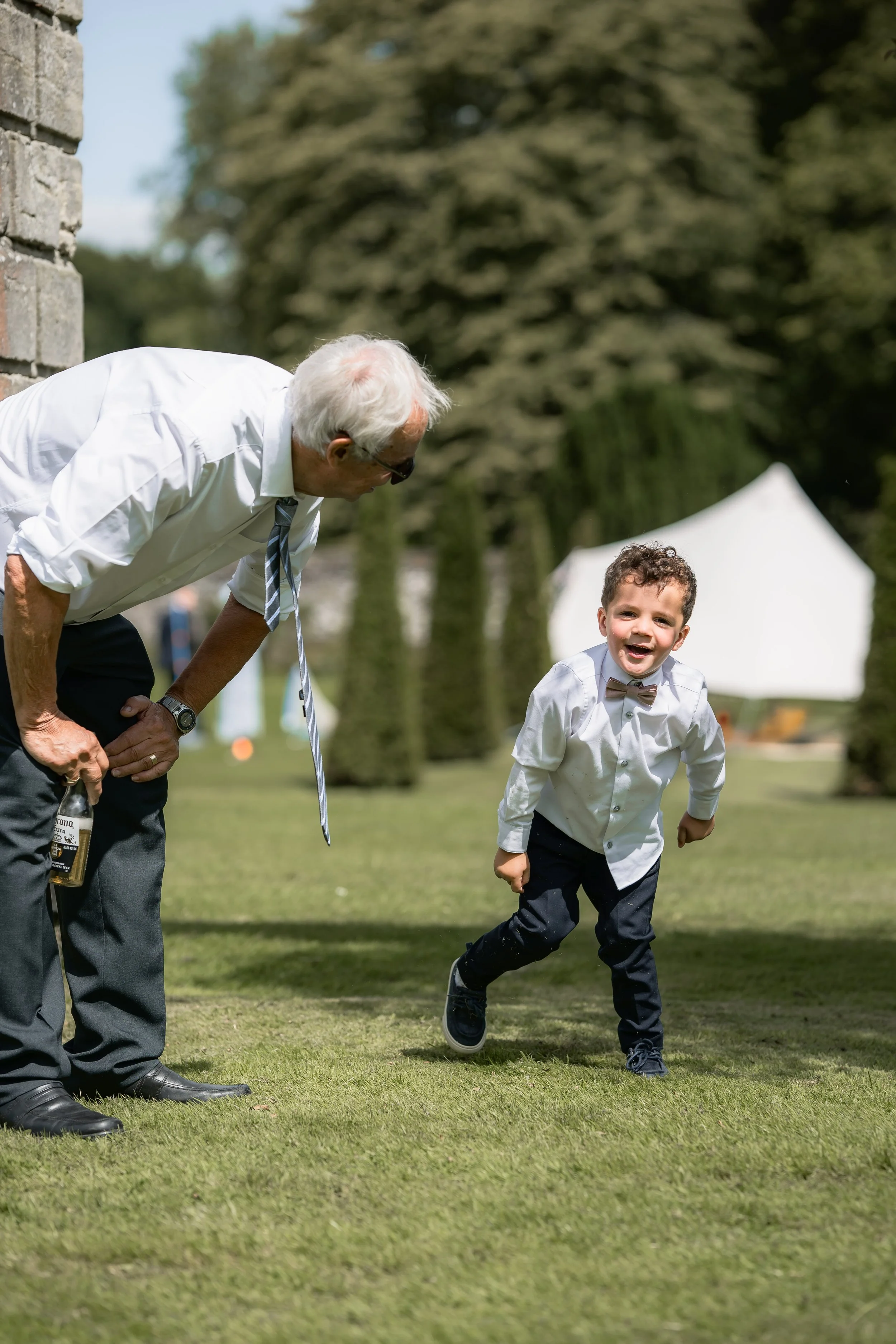 An elderly man and a young boy in formal attire, both with bow ties, playing outdoors on a grassy lawn during the day.
