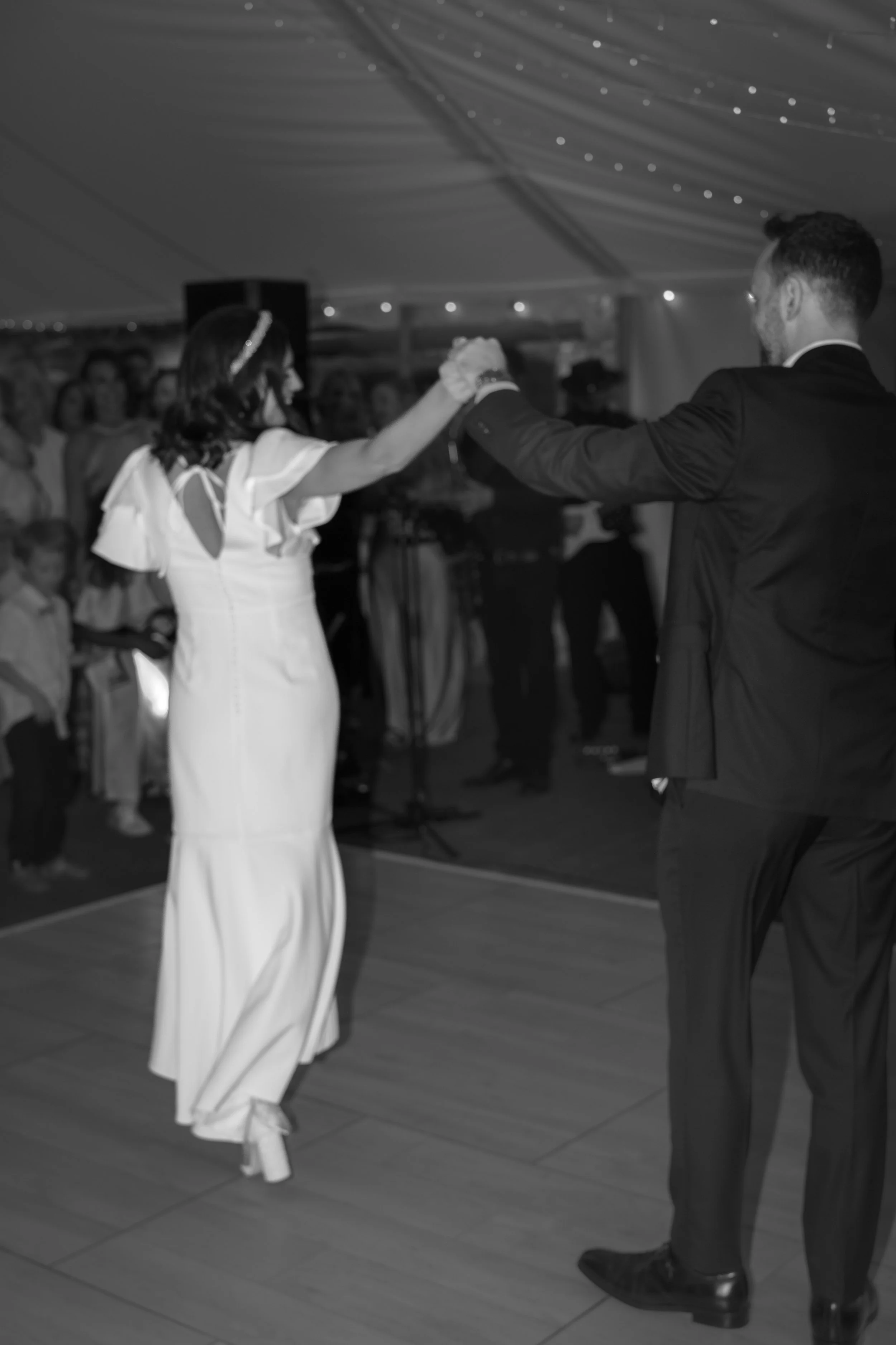 A bride and groom dancing together at their wedding reception, with guests watching in the background.