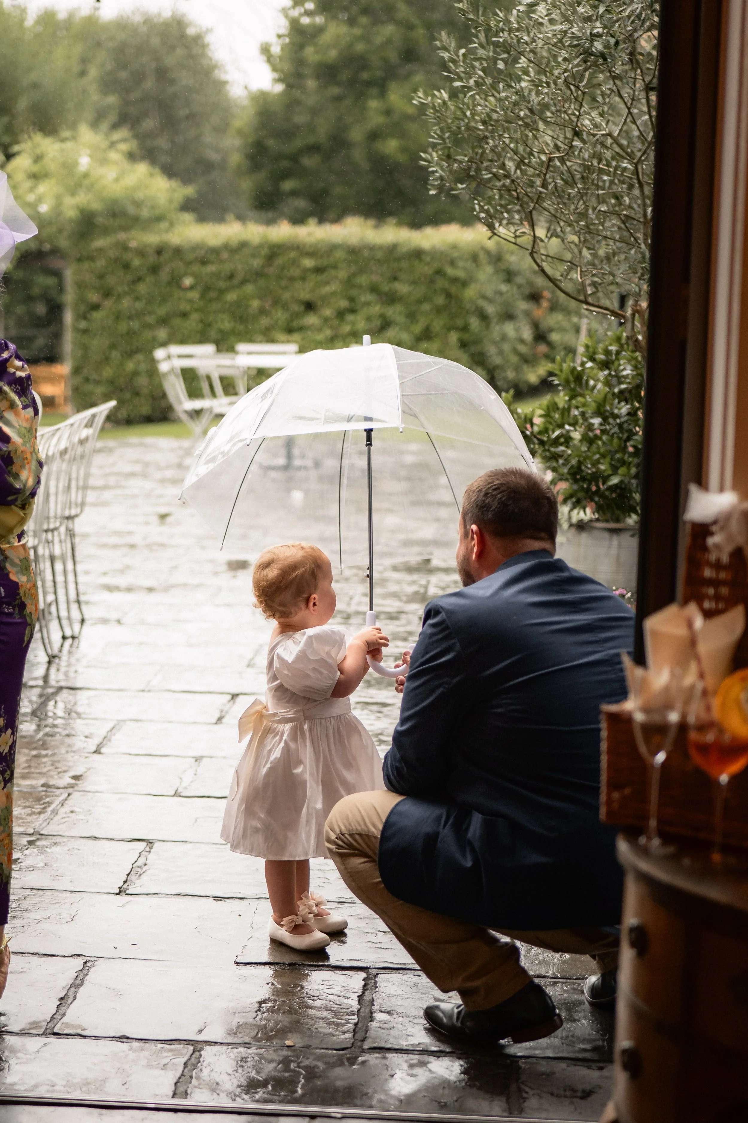 A man kneeling outside holding a young girl with an umbrella during rainy weather at an outdoor event.