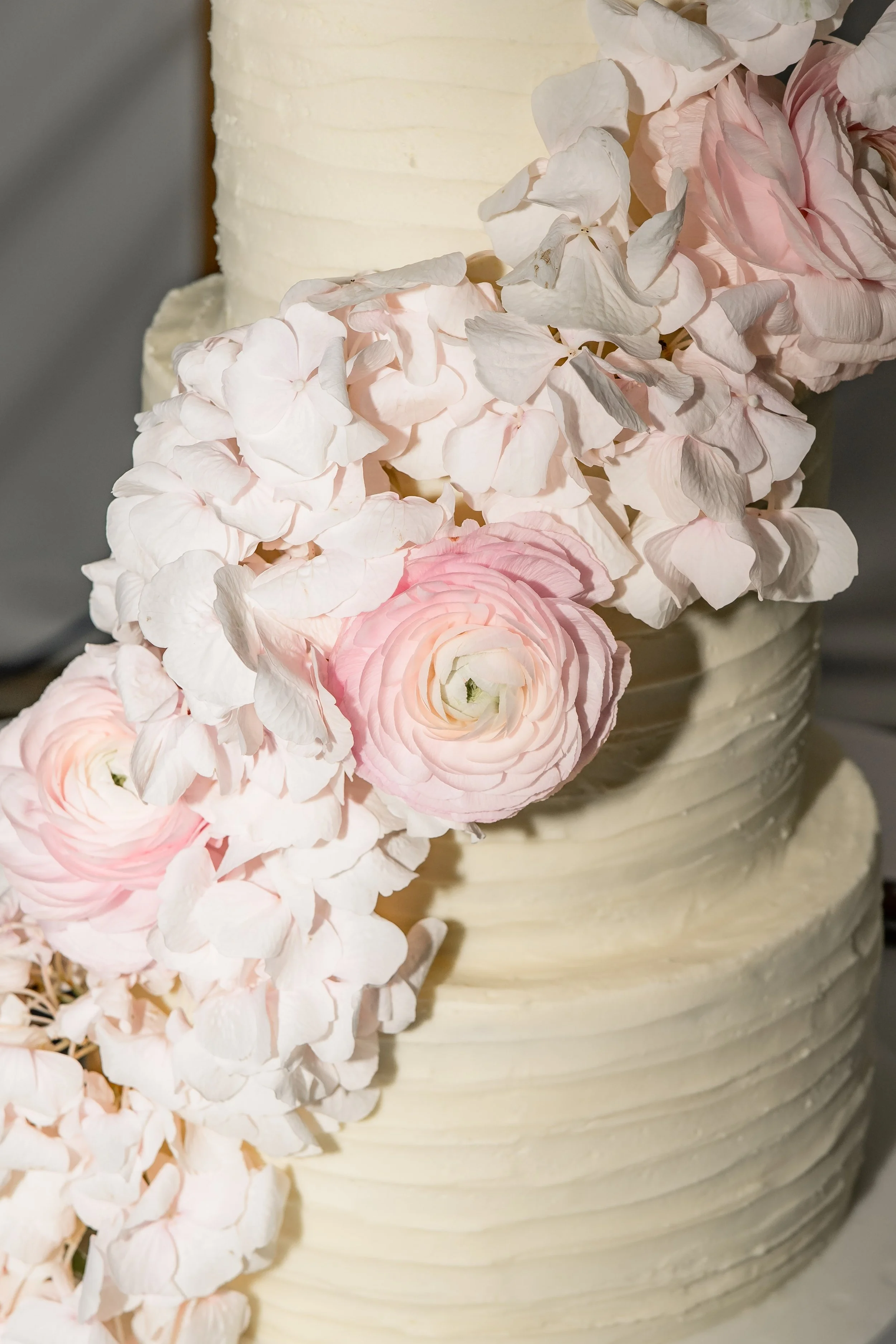 Close-up of a wedding or celebration cake decorated with white and pink hydrangeas and ranunculus flowers.