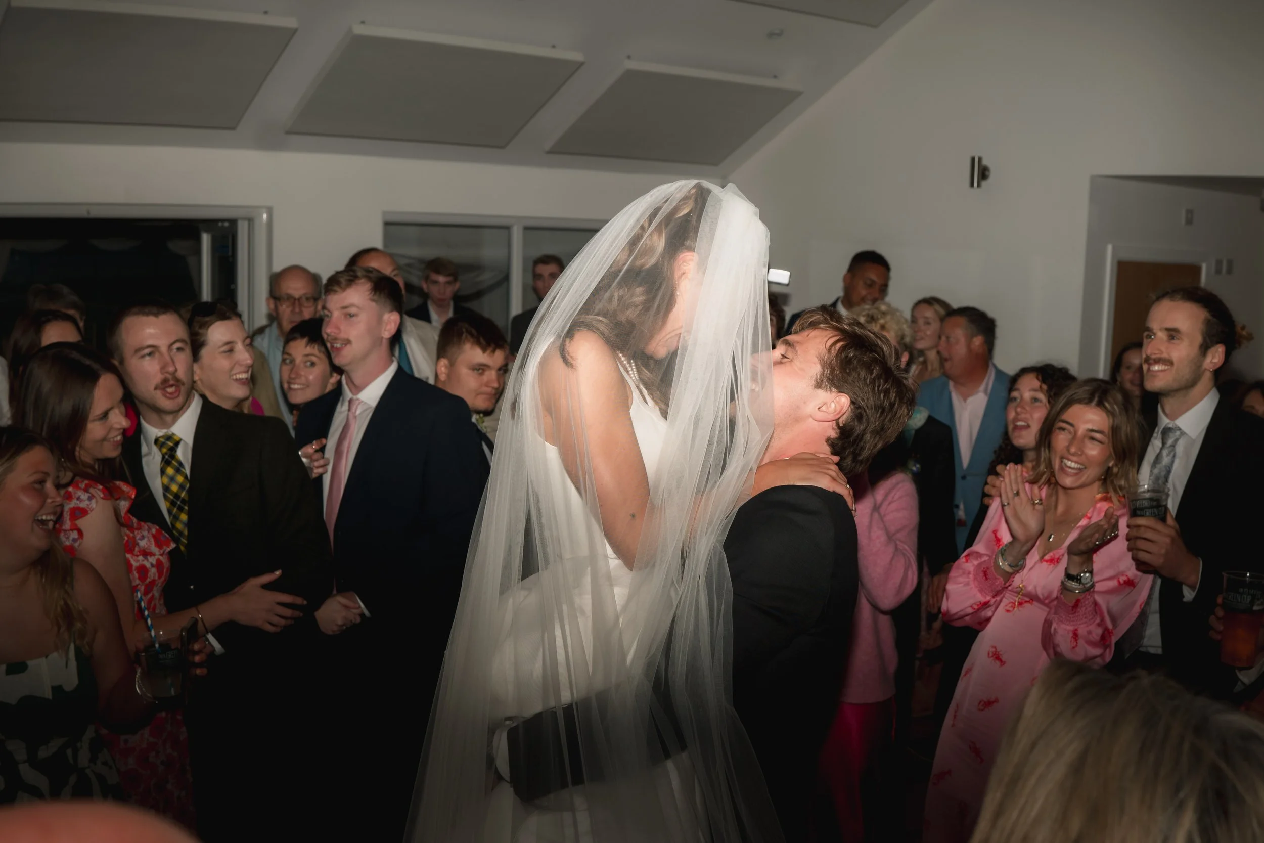Bride and groom sharing a kiss in front of wedding guests at a celebration reception.