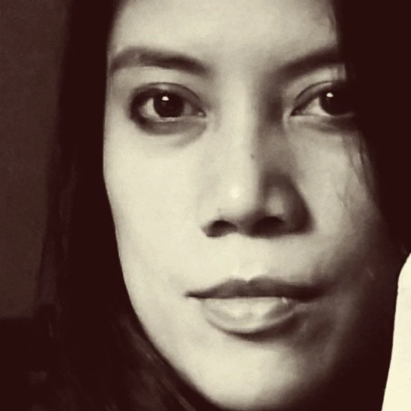 Close-up black and white photo of a woman's face with dark hair and expressive eyes.