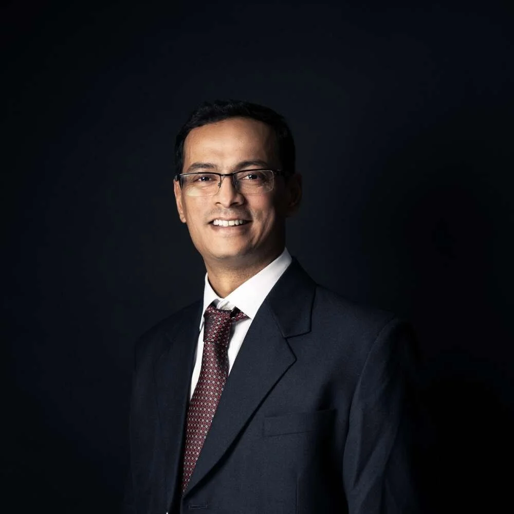 Professional man in a suit and tie smiling against a dark background.