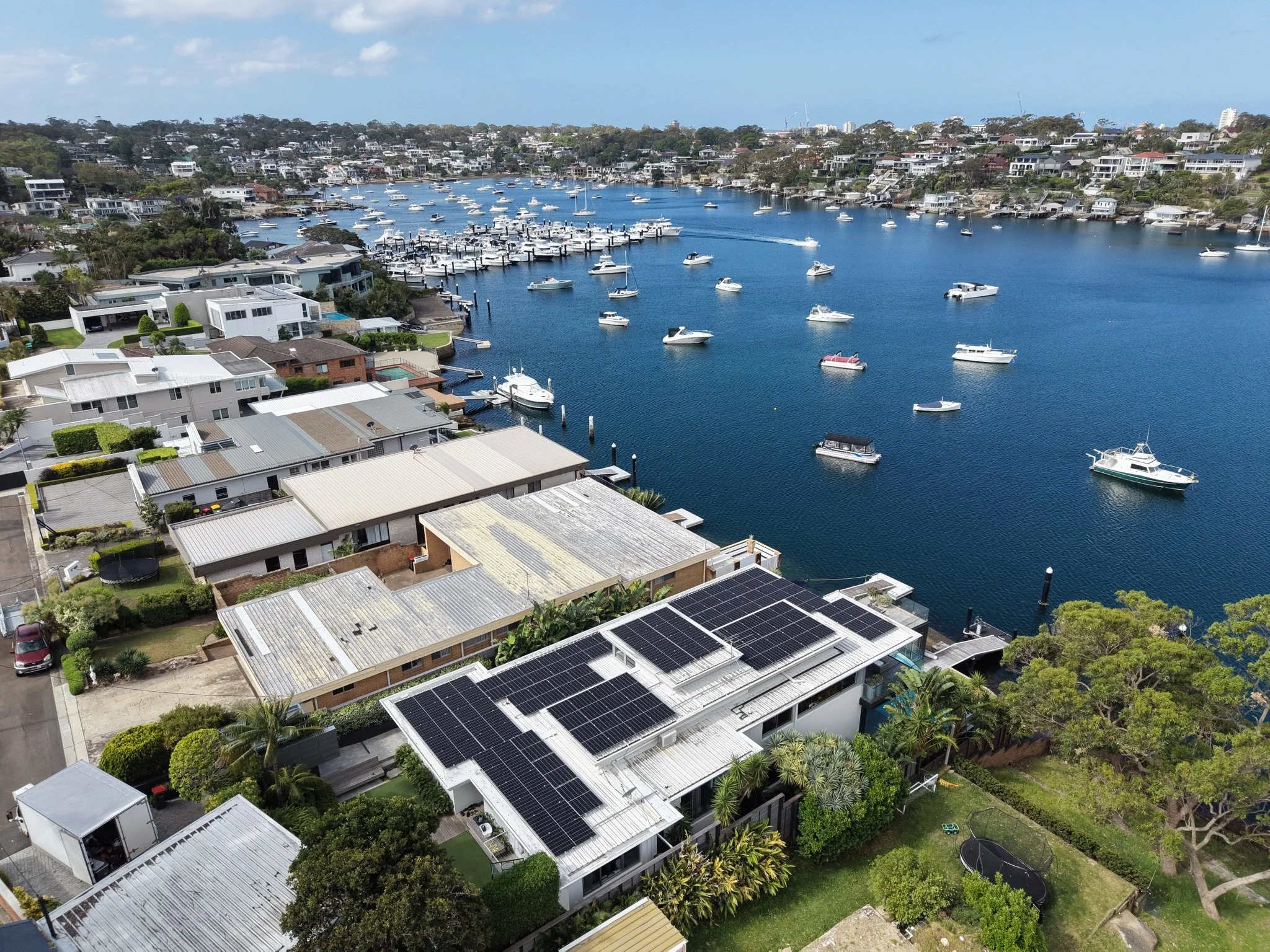 Aerial view of a residential neighborhood by a marina with boats on the water; homes have solar panels on their roofs.