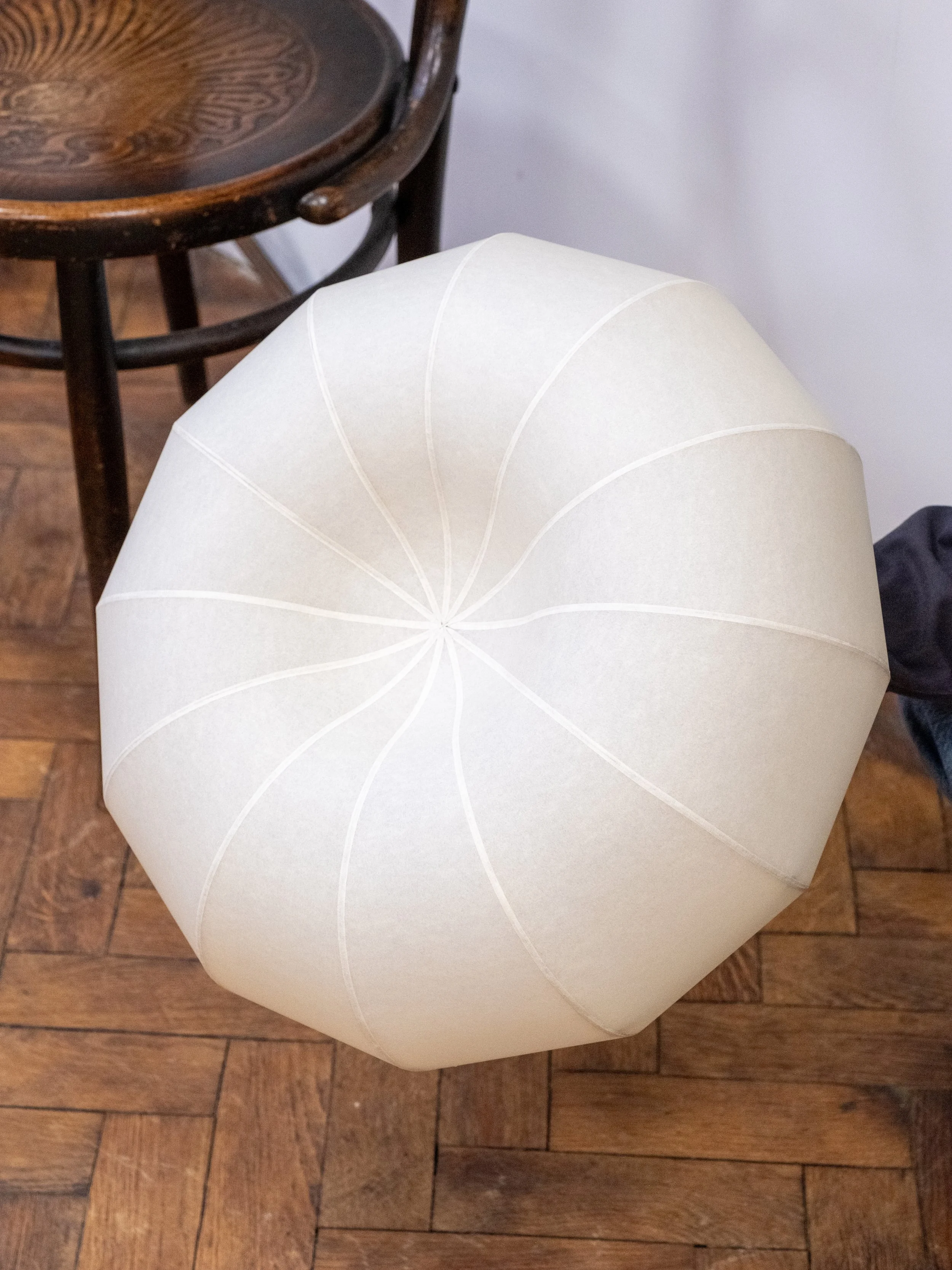 Small version of the Plumus Pendant Light by Claud Christian, a sculptural paper pendant with organic curved design, styled in a contemporary interior above a parquet floor.