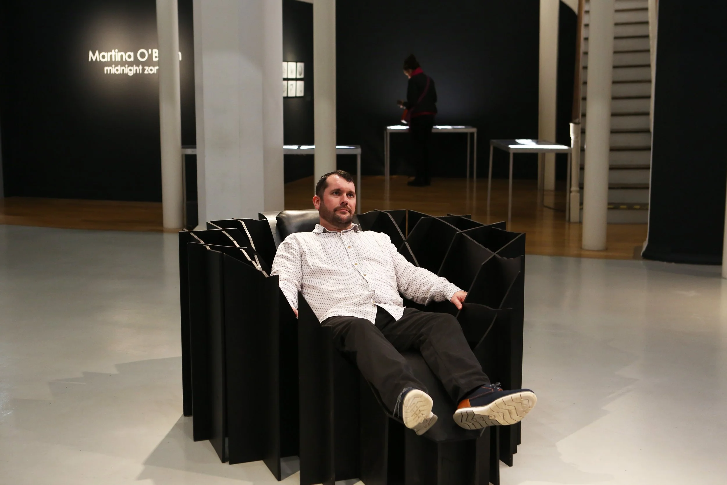 Eoghan+in+the+%27chair%27+close-up+with+exhibition+title+in+the+rear+-+landscape.png