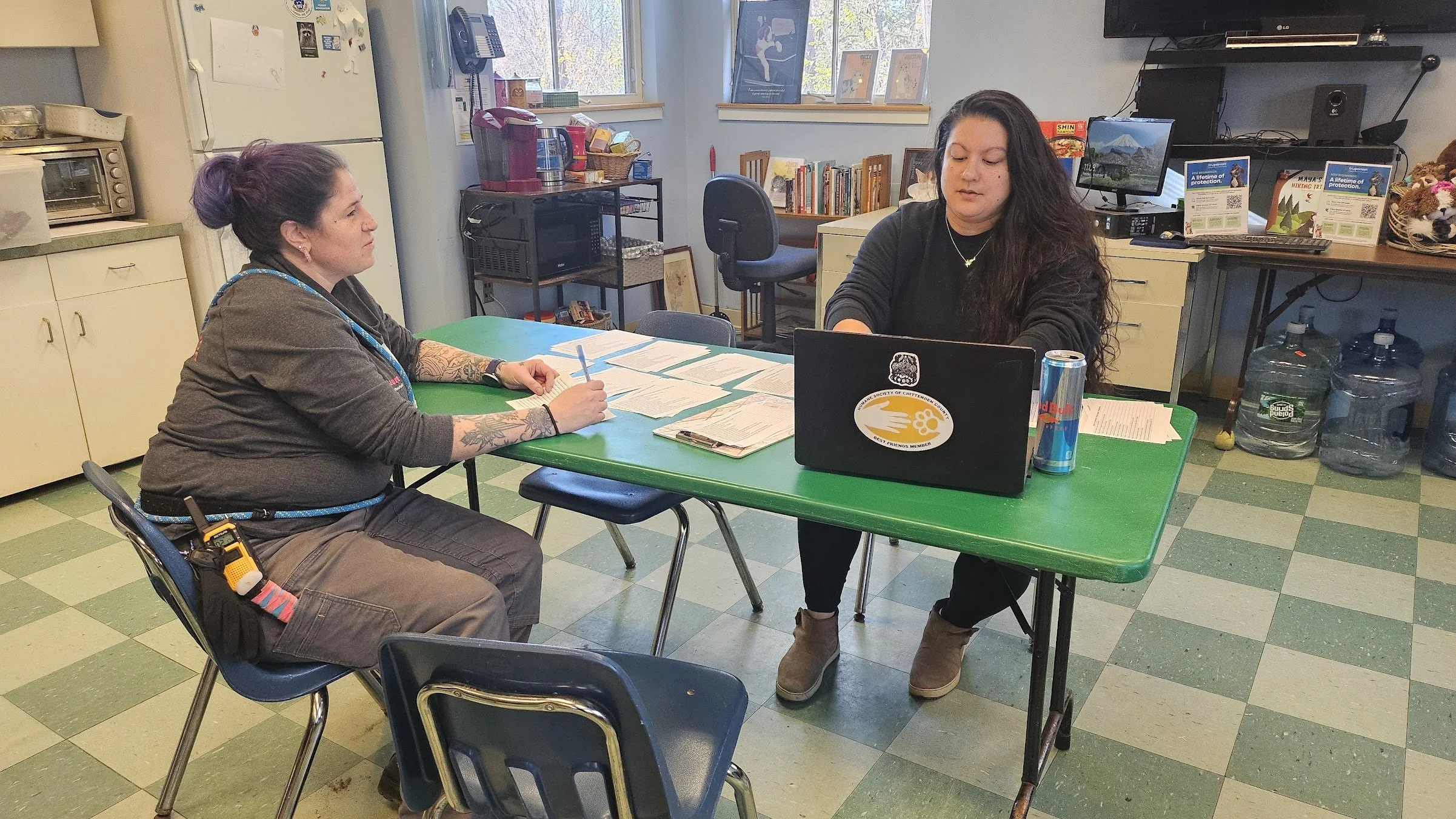 Laurie Lawless (left) sits diagonally across a table with a shelter worker (right). The green table is scattered with papers and a computer.
