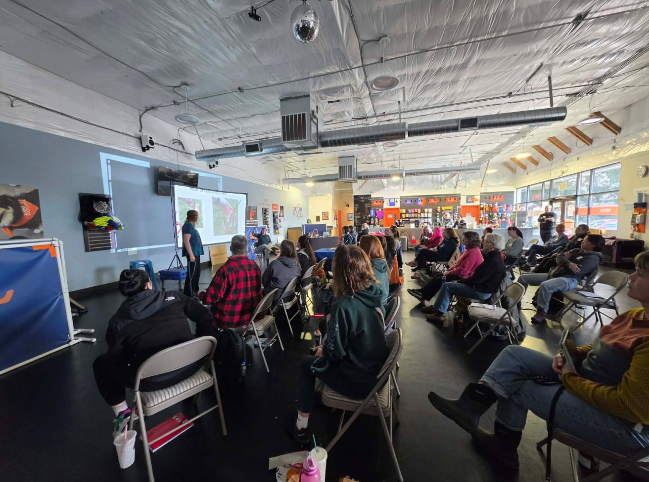 Shelter staff and volunteers sit arranged on chairs in a large room watching a training presentation.