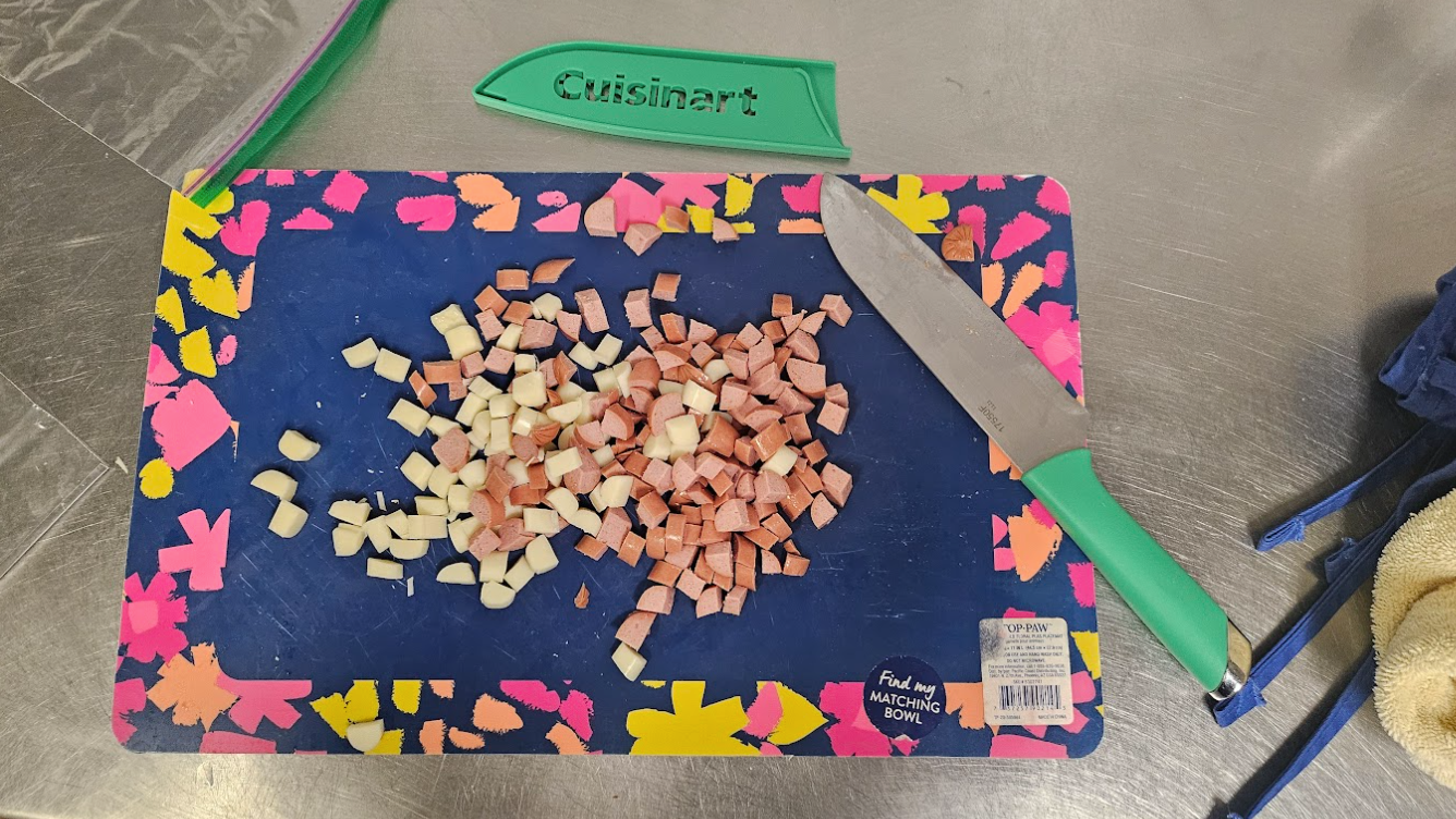 A variety of cubed cheese and sausage sits on a blue cutting board with pink and yellow flowers around the perimeter.