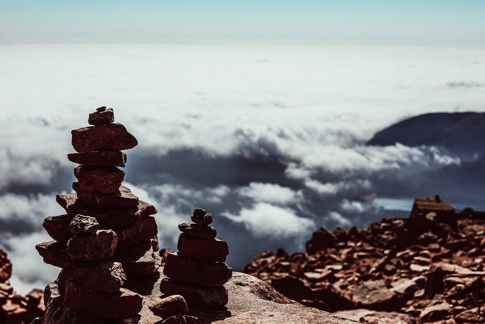 Stacks of rocks on a mountain with a cloudy sky and mountain in the background.