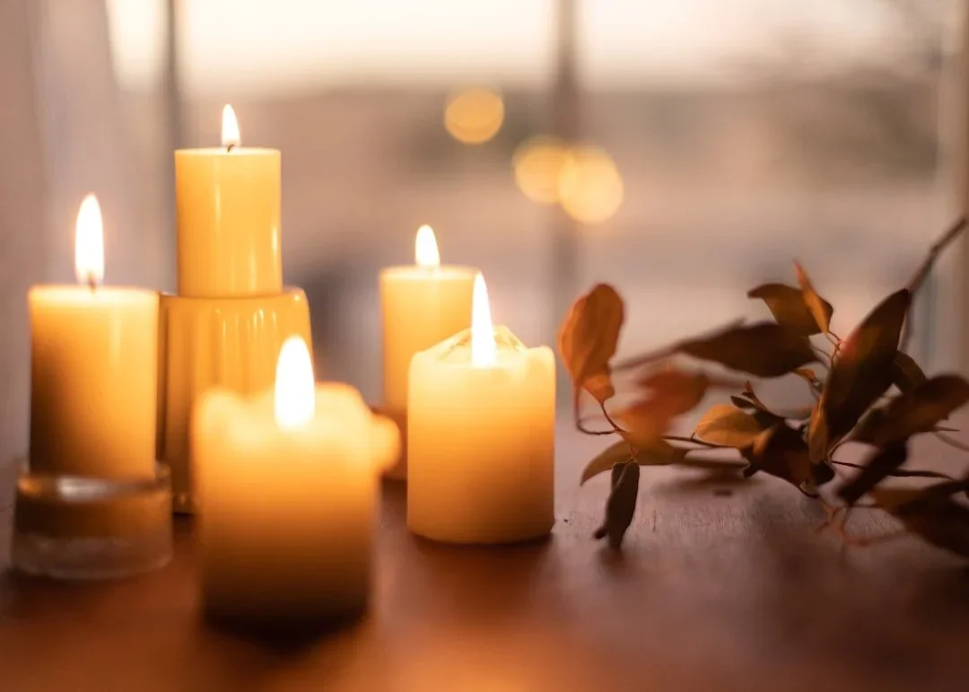 Five lit yellow candles and a bunch of dried leaves on a wooden surface.