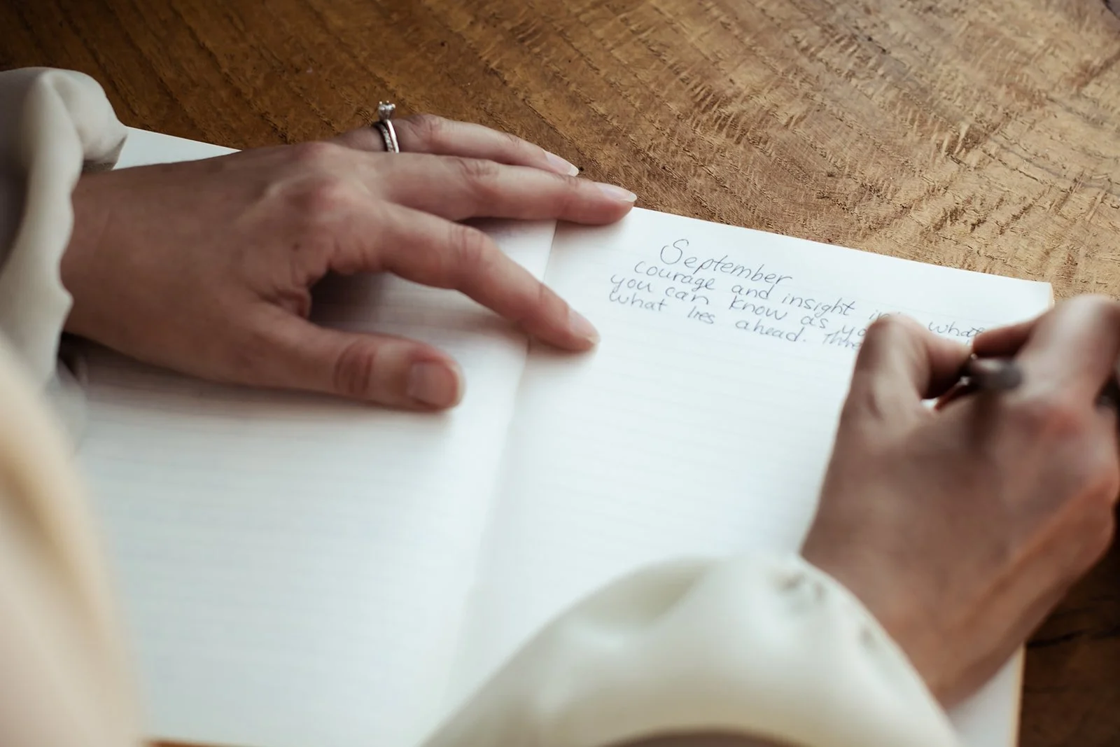 A person writing in a notebook with handwritten notes about September, courage, and insight on a wooden table.