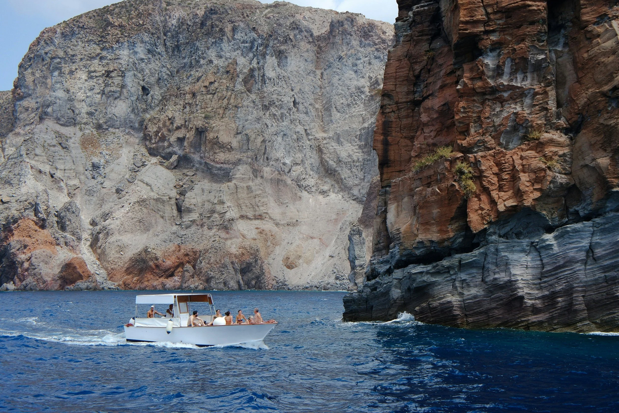 A boat with people in a canyon with tall, rugged cliffs and deep blue water.