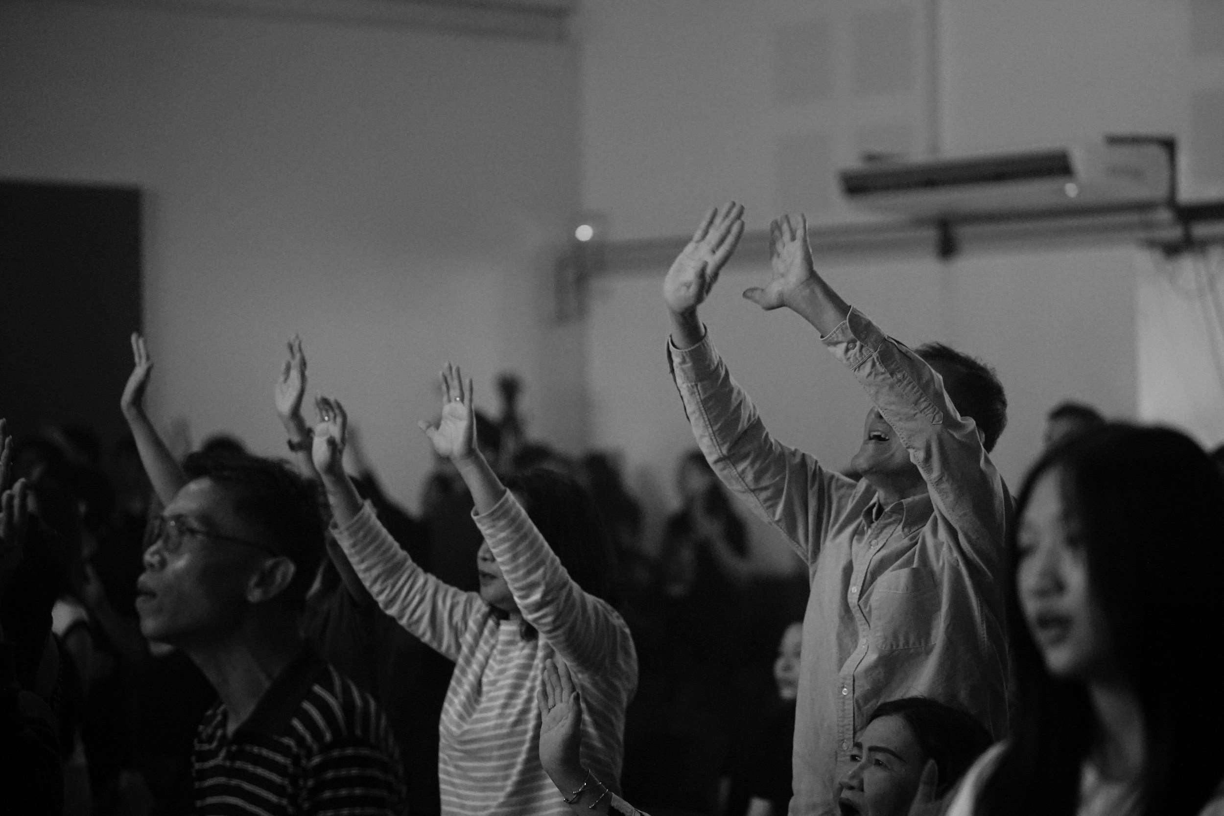 black and white photo of people with hands raised in worship