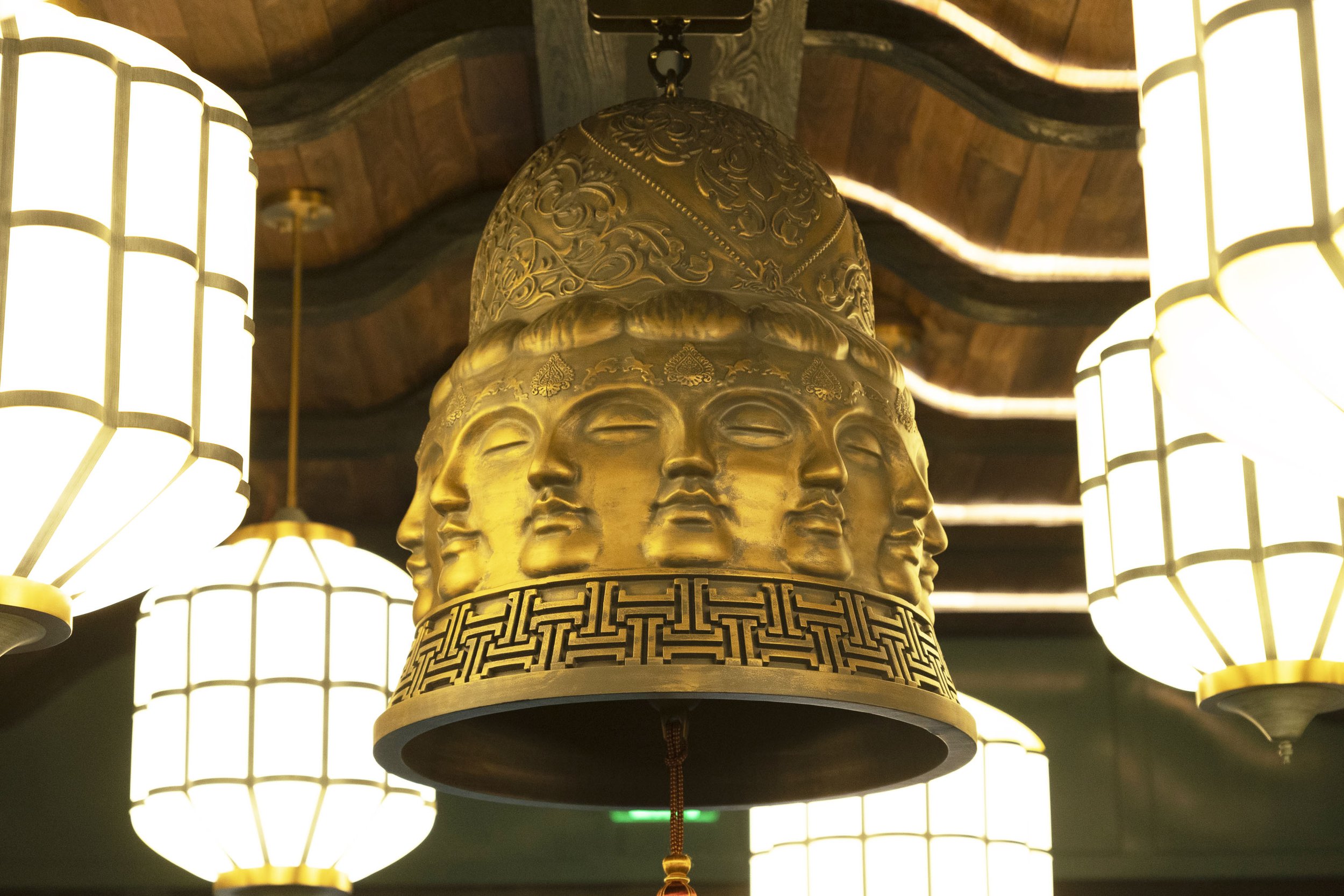 Golden decorative hanging lantern featuring multiple human faces and intricate patterns, illuminated by surrounding traditional paper lanterns.
