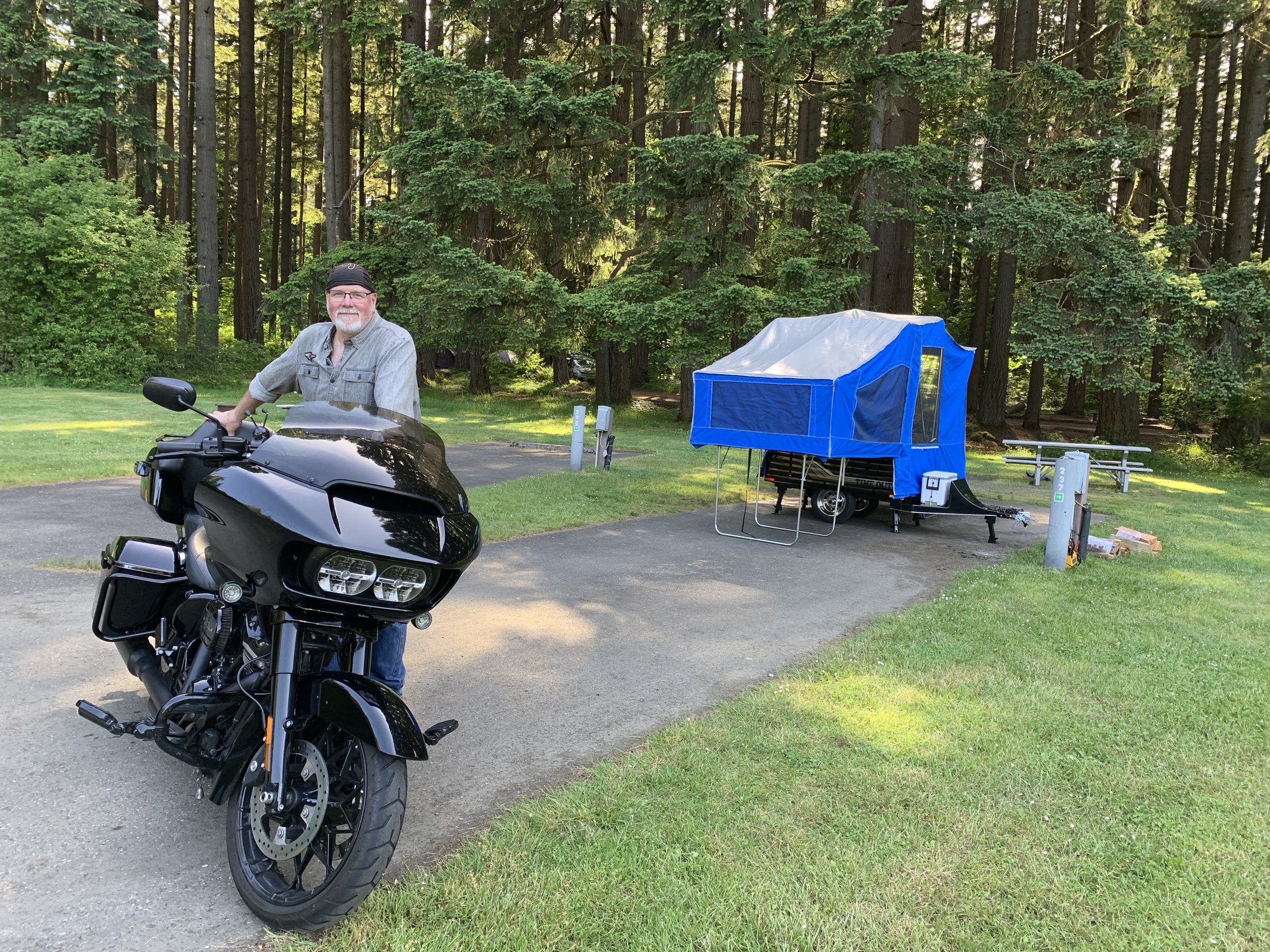 Dave the Buddha Biker standing next to his Harley  Davidson Road Glide with Time Out Deluxe camper  trailer at Millersylvania State Park near Olympia  Washington