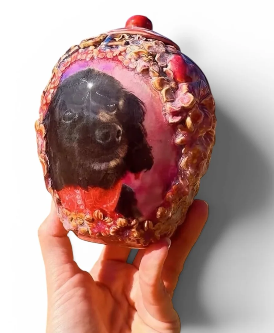 Hand holds a large custom dog urn with a picture of a black dog printed on its surface. made by Arist Tara Hinkley