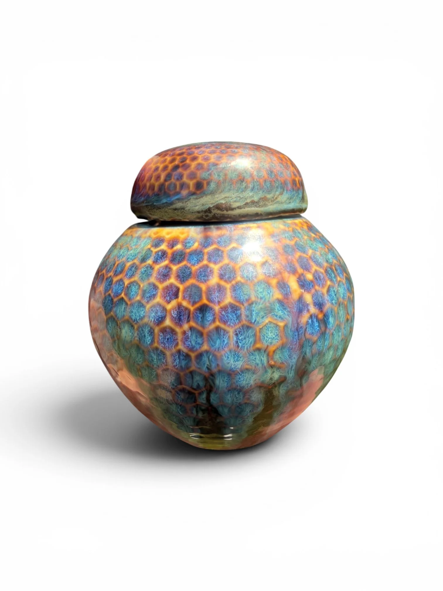 A ceramic vase with a rounded body and a smaller rounded lid on top, featuring a colorful hexagonal pattern in shades of blue, orange, and purple with an iridescent sheen.