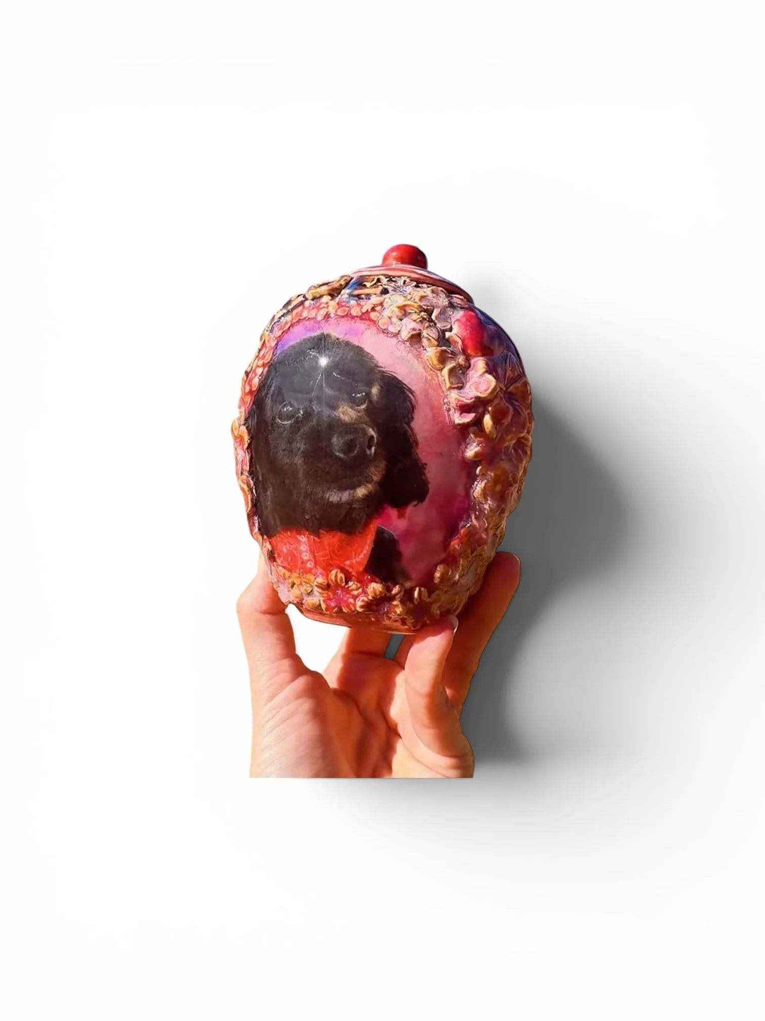 A hand holding a strawberry with a printed image of a dog on its surface. The dog appears to be a black puppy with dark fur, looking directly at the camera.