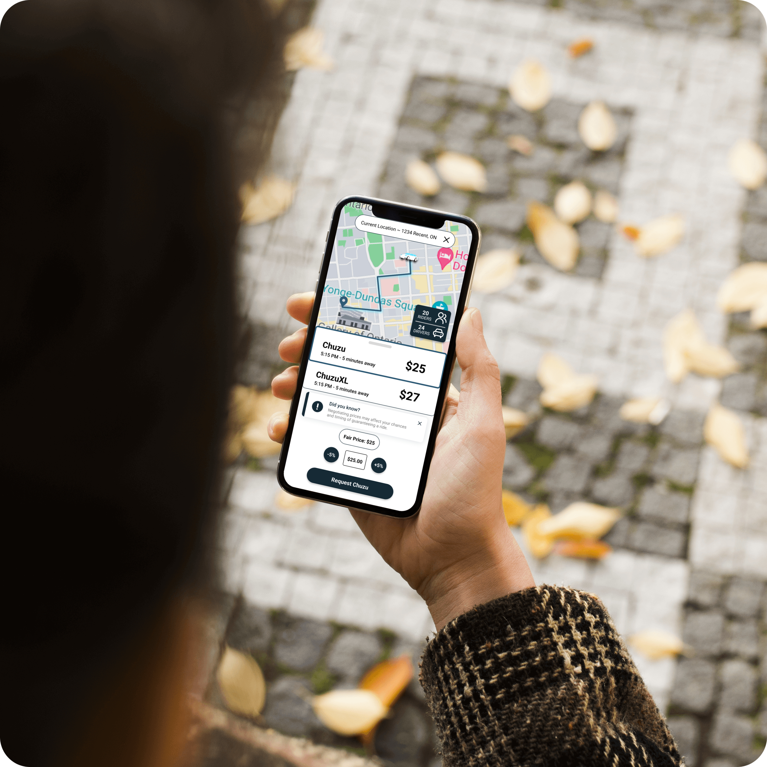 Person holding a smartphone displaying a ride-sharing app with a map and ride options on a cobblestone path with fallen leaves.