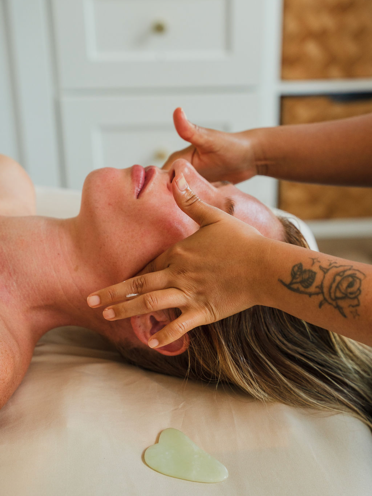 Person receiving a facial massage with massage oil on a massage table in a spa setting.