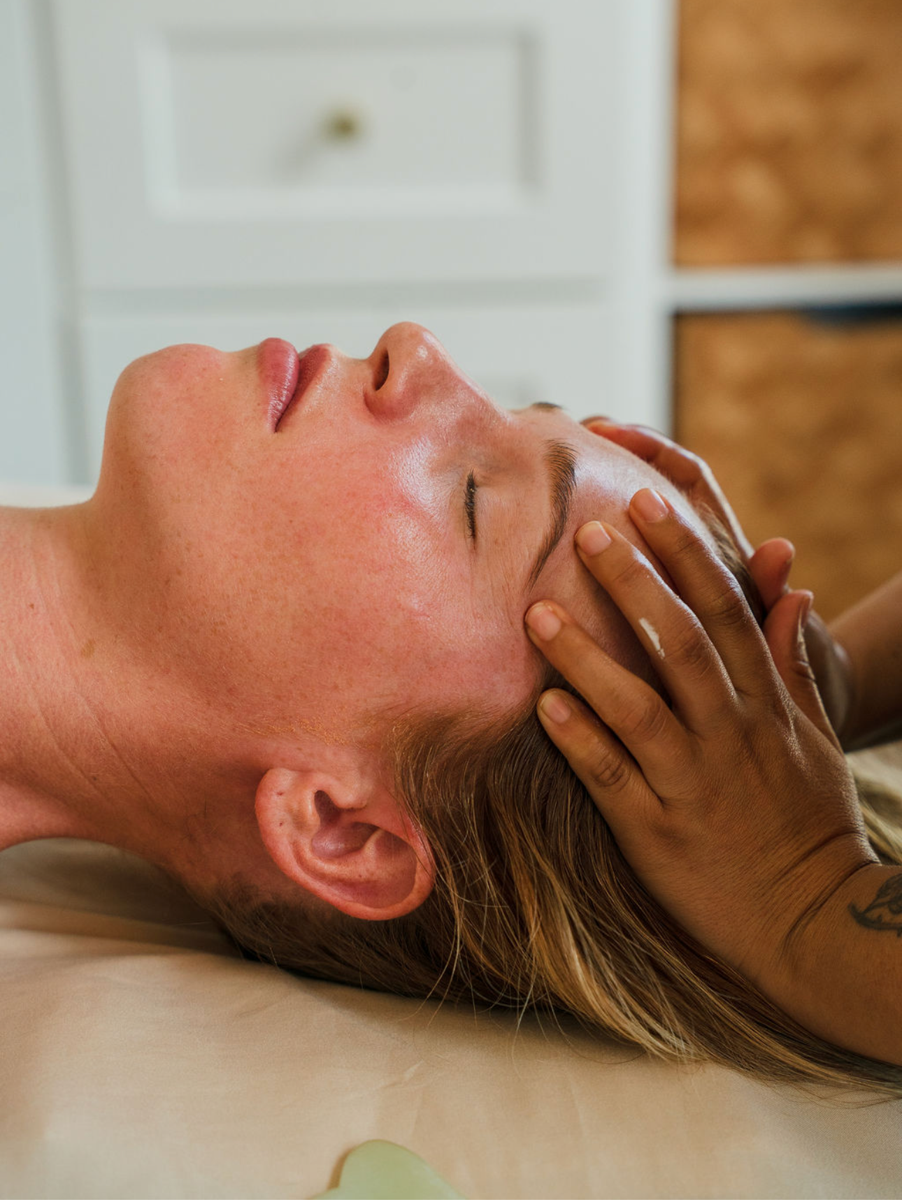 A person receiving a facial massage from a massage therapist in a spa or treatment room.