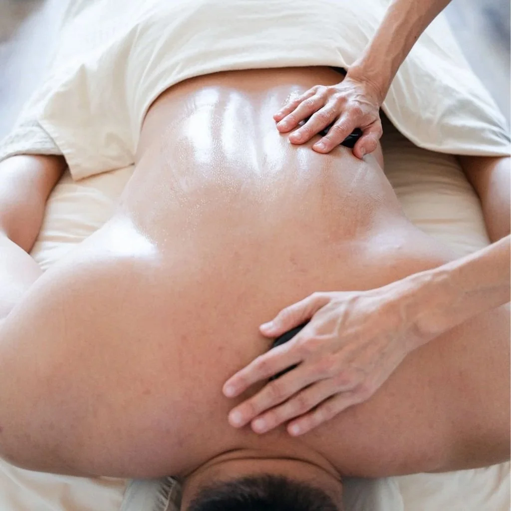 A person lying face down on a massage table, receiving a back massage, with oil applied to their back.