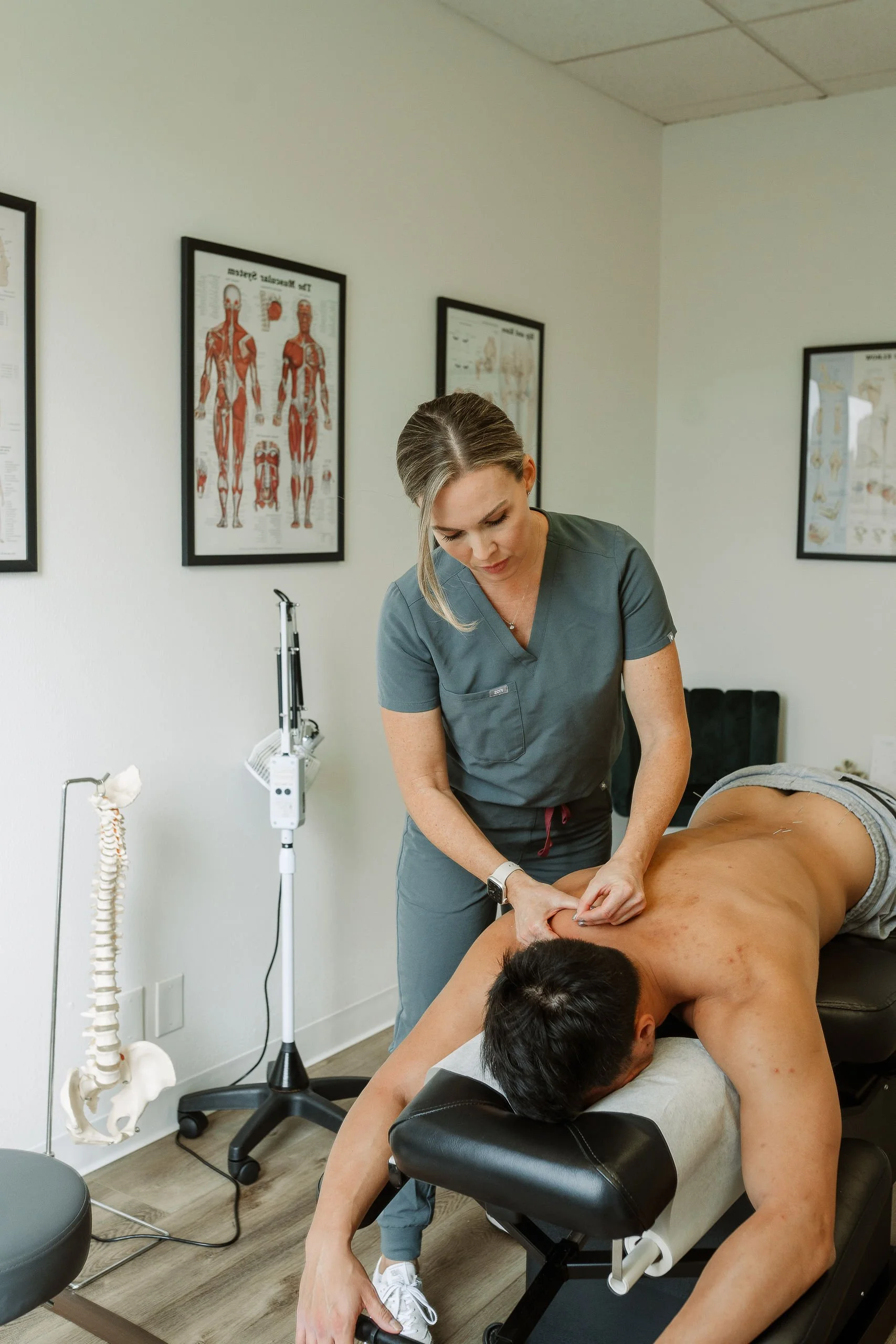 Chiropractor performing an adjustment on a male patient lying face down on a chiropractic table in a medical office.