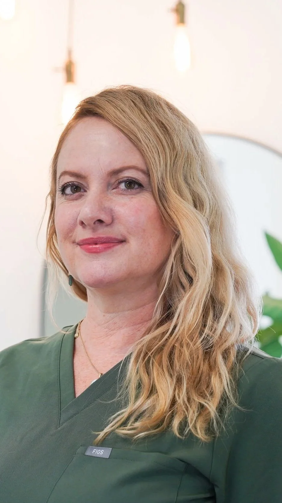 Smiling blonde woman in dark green medical scrubs with a FIGS name tag
