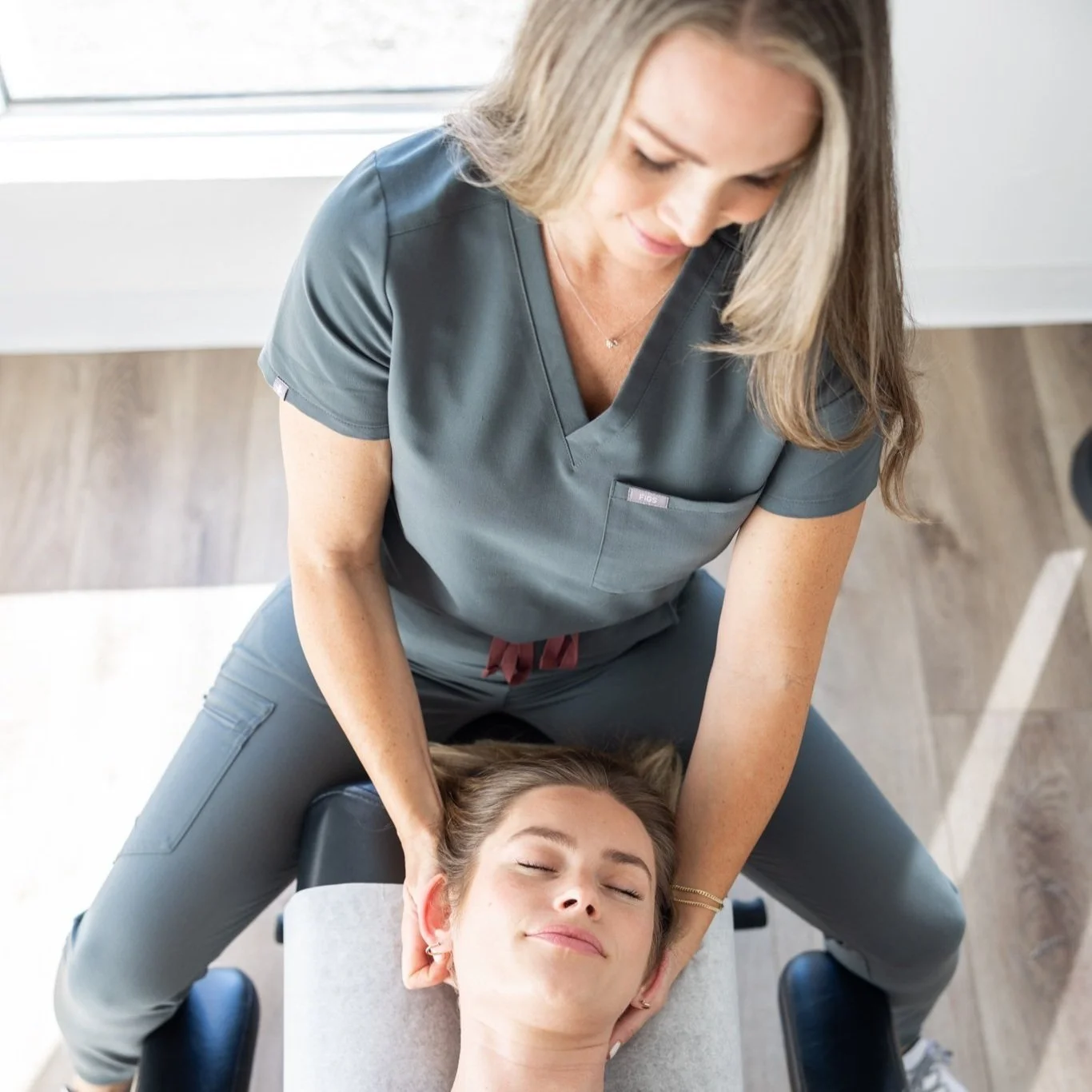 Chiropractor performing neck adjustment on a woman lying face-up on a chiropractic table.