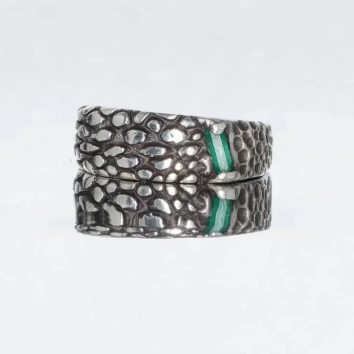 Metal textured ring with a green stripe, reflected on a smooth surface.