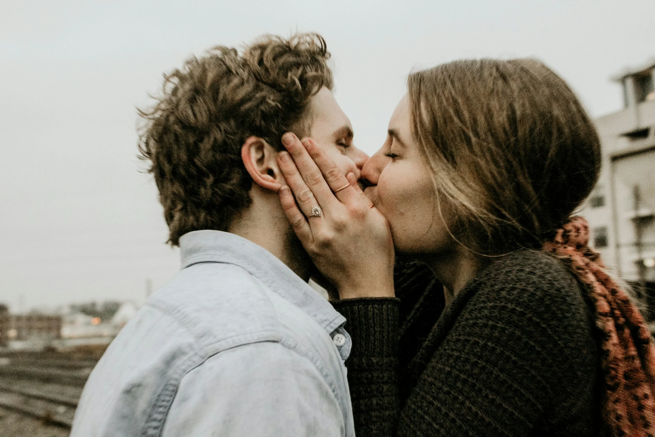A 30-something white man and woman kiss passionately. Seen from profile angle. Nondescript background.