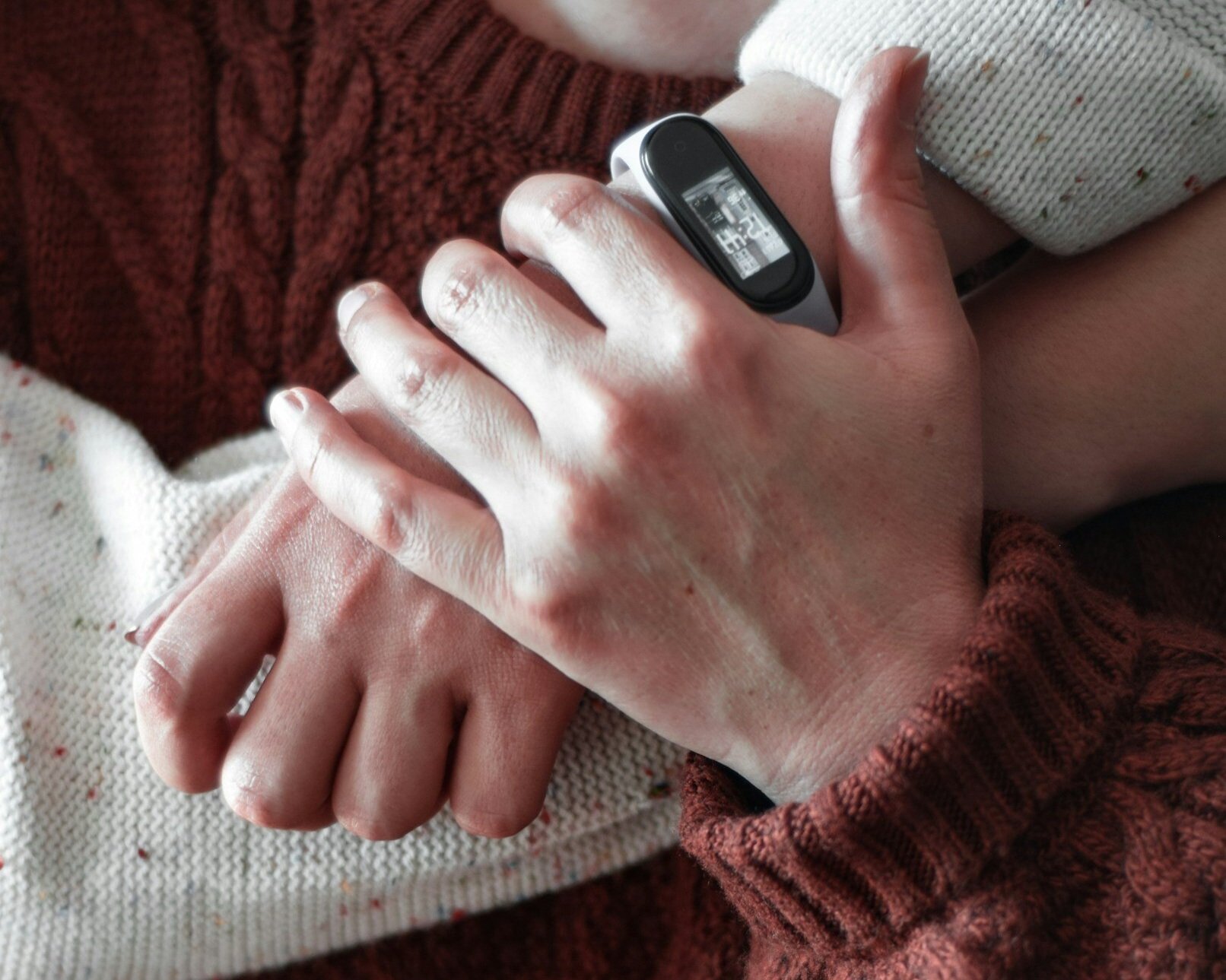 Hands of two white people embracing over the chest of one person. Each wearing sweaters, one wears a watch.